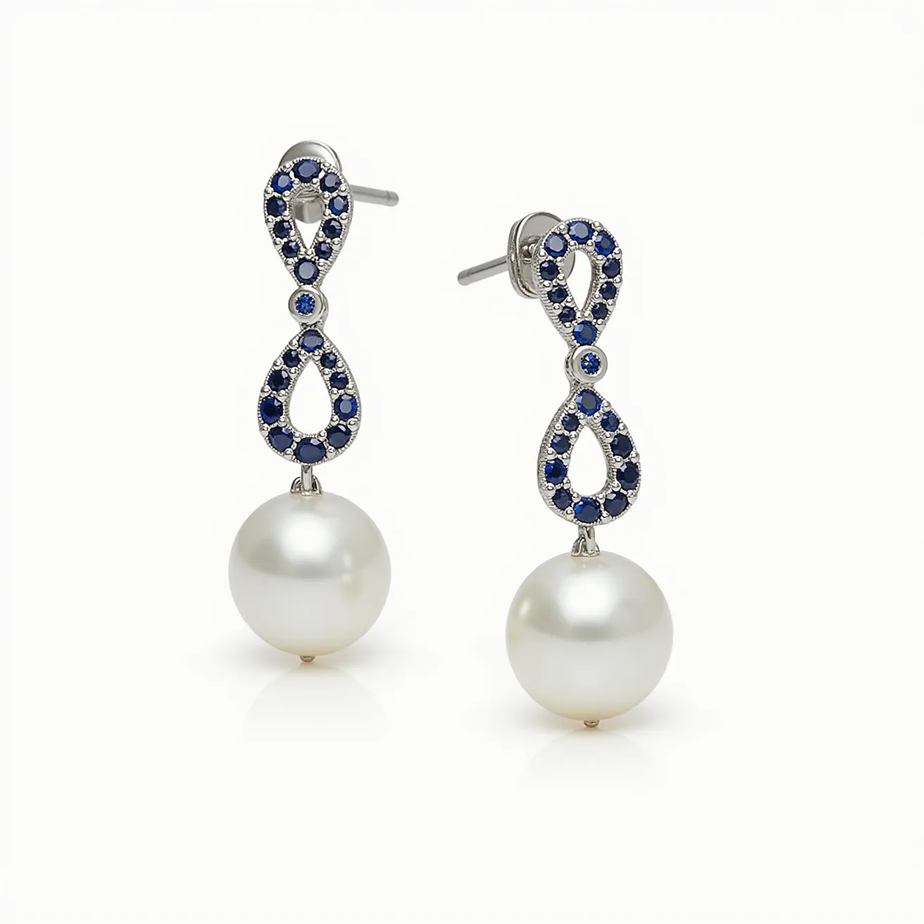 These pearl drop earrings feature a classic design, combining lustrous white pearls with an elegant metal setting. The earrings are adorned with deep blue gemstones, possibly sapphires, that are precisely cut and set into an infinity loop design. The stones are surrounded by a metal that complements the overall aesthetic. The earrings are attached with a stud post and butterfly back, ensuring a secure wear. The combination of pearls and blue gems adds a touch of sophistication and elegance to the piece.