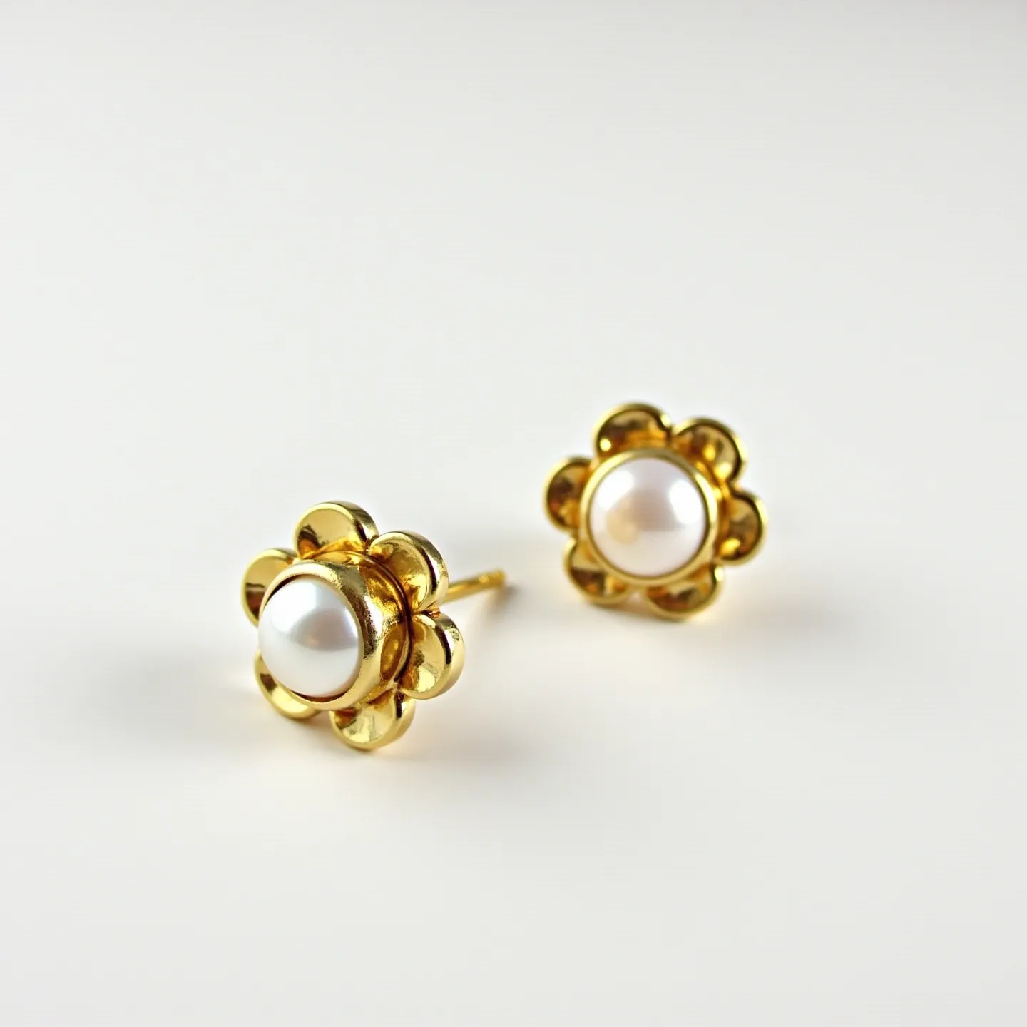 These pearl stud earrings feature a central round pearl, elegantly set within a gold-colored floral setting. The petals encircle the pearl, creating a balanced and harmonious design. The attachment is a traditional post, suitable for pierced ears, ensuring a secure fit. The gold surrounding the pearl enhances its lustrous quality, while the simple yet sophisticated design makes the earrings versatile for various occasions.