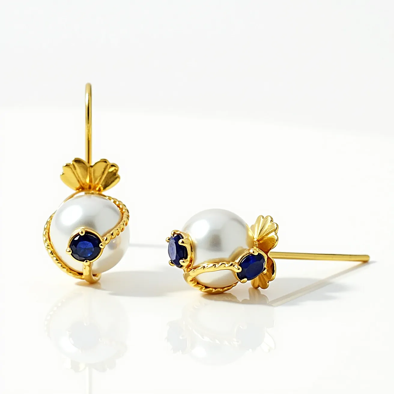 These pearl stud earrings feature elegant white pearls as the centerpiece, accentuated by a gold setting that adds a luxurious touch. The design incorporates small, round blue gemstones, likely sapphires, which are set into a delicate gold bezel. The beads are further enhanced by gold leaf motifs that wrap around the pearls, adding an artistic and graceful element to the design. The attachment is a post back, ensuring a secure and comfortable fit when worn. These earrings offer a classic yet sophisticated look, suitable for a variety of occasions.