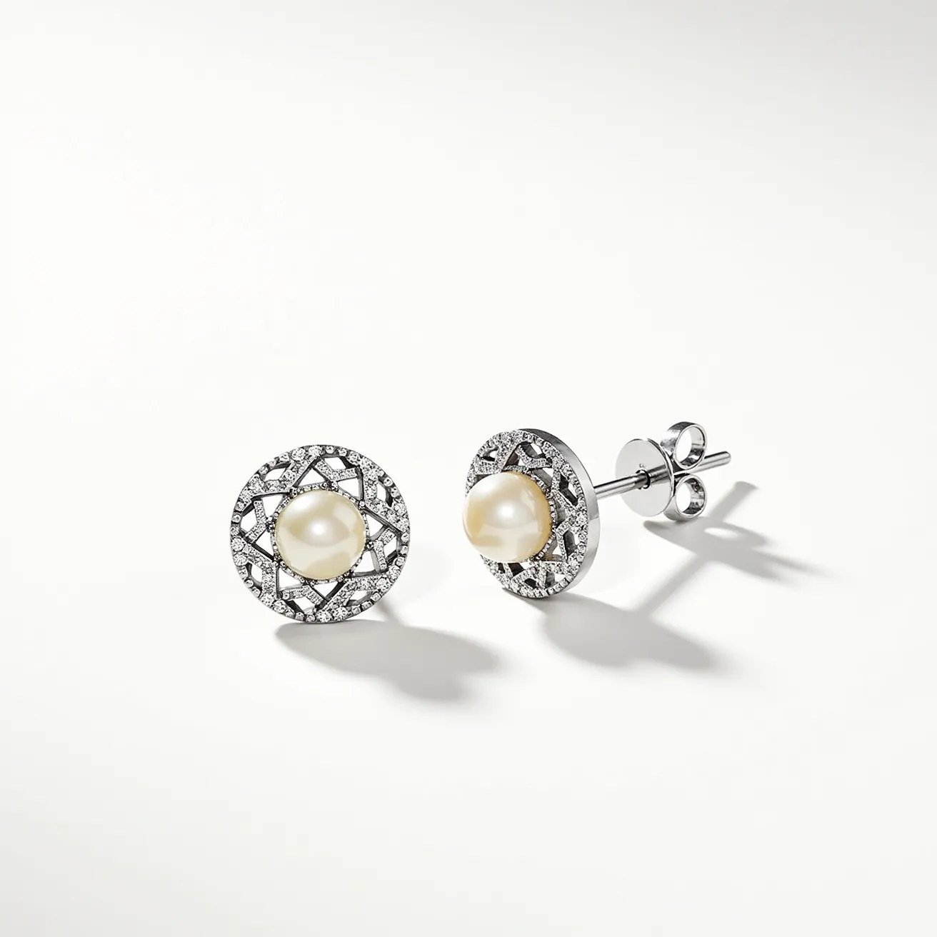 These pearl stud earrings feature a central, lustrous pearl set within a circular frame. The frame is crafted from a shiny metal, likely sterling silver or white gold, intricately designed with small, sparkling gems. These gemstones appear to be diamonds, set in a pavé style that enhances the overall brilliance of the earrings. The attachment features a classic post and butterfly clutch back, ensuring a secure fit for the wearer. The combination of the pearl's gentle glow and the diamonds’ sparkle creates an elegant and timeless design.