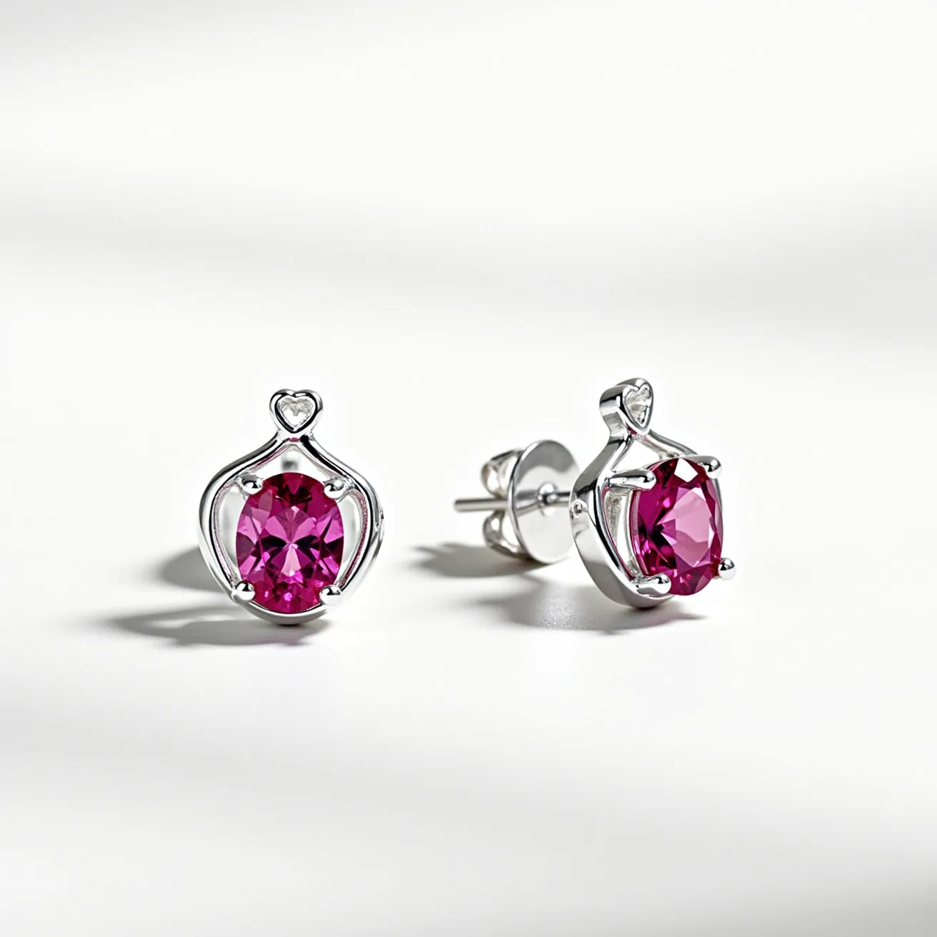 These pink earrings feature a striking design with round-cut pink gemstones set in a four-prong silver setting, creating an elegant and modern look. The gems are centrally positioned and surrounded by a decorative silver element that incorporates a small heart motif at the top, adding a touch of romance to the overall appearance. The earrings are attached using a post and butterfly clasp, ensuring they are secure when worn. The combination of vibrant pink stones and shiny silver metal creates a visually appealing contrast, making these earrings both stylish and versatile.