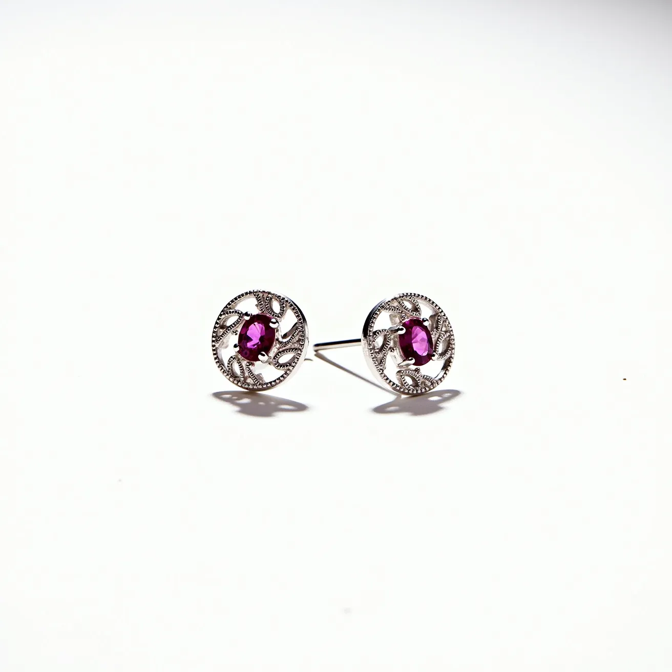 These pink earrings showcase a vibrant pink gemstone, which appears to be oval-cut, centrally set in a detailed, circular silver frame. The silver material is intricately designed with a pattern that enhances the elegance of the piece. The gemstone is likely a synthetic or natural stone known for its pink hue, securely fastened within a bezel or prong setting that highlights its shape and color. These earrings use a post and butterfly clasp attachment, allowing for secure and comfortable wear.