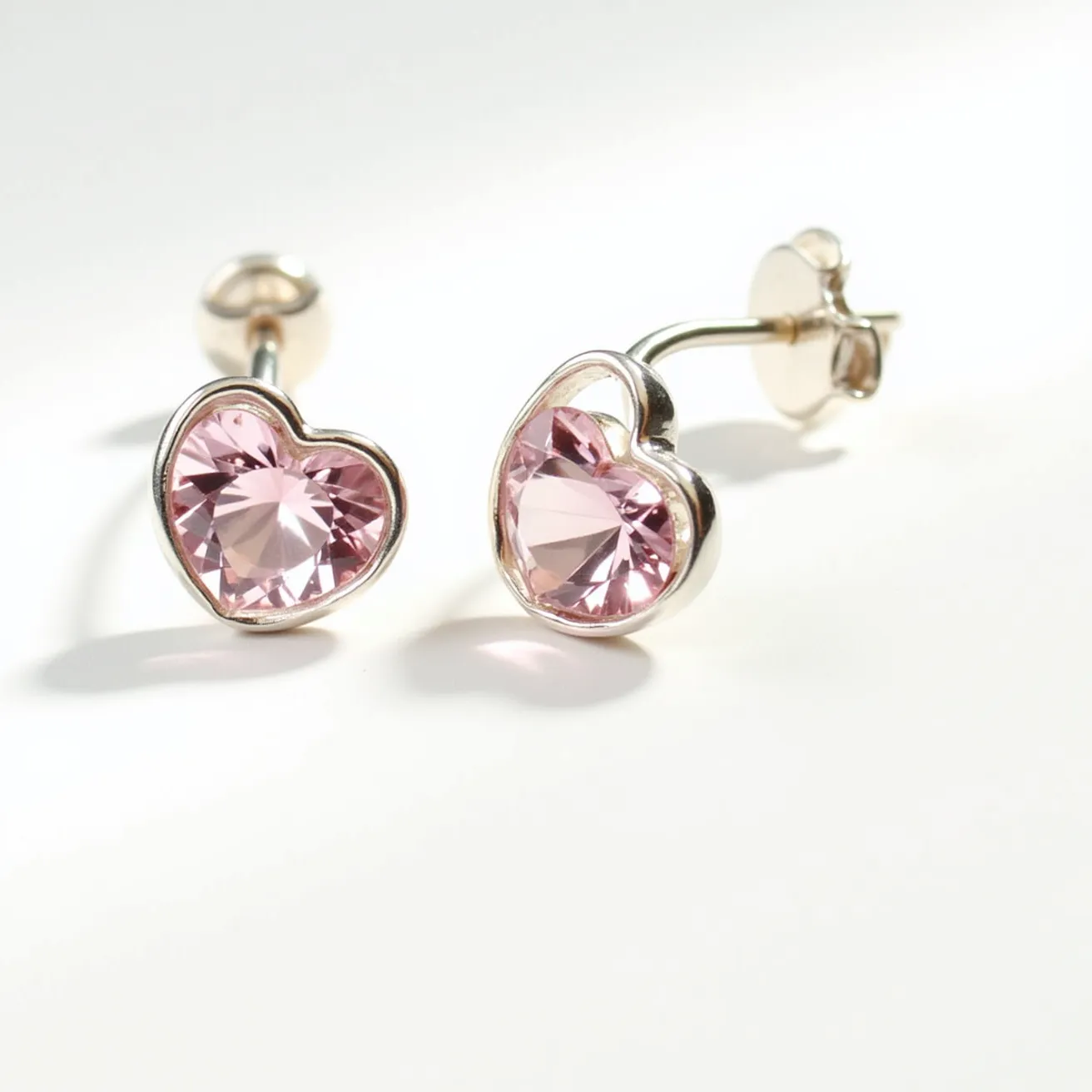 These pink earrings feature heart-shaped pink stones that are likely faceted for added brilliance. The stones are set within a polished metal frame that appears to be silver or white gold, providing a smooth and reflective surface that enhances the overall shine. Each earring is designed with a stud post and secured with a butterfly clasp, ensuring they stay comfortably in place when worn. The design combines elegance with a playful touch, making them a versatile accessory.