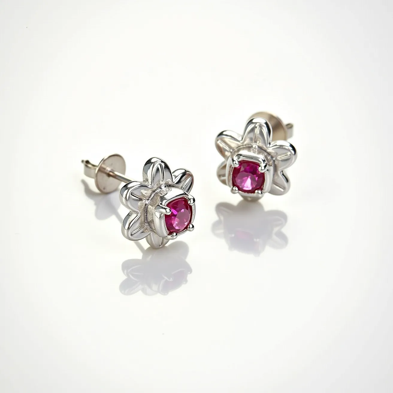 These pink earrings feature vivid pink gemstones, likely rubies, set in a floral motif. The stones are round-cut and held securely by a prong setting, enhancing their brilliance and visibility. The metal appears to be polished silver or white gold, adding a sleek, modern contrast to the vibrant stones. The earrings are designed with a stud attachment and are secured with a friction back, ensuring comfort and ease of use while wearing. The elegant design combines classic gem settings with a playful floral shape, making them versatile for various occasions.