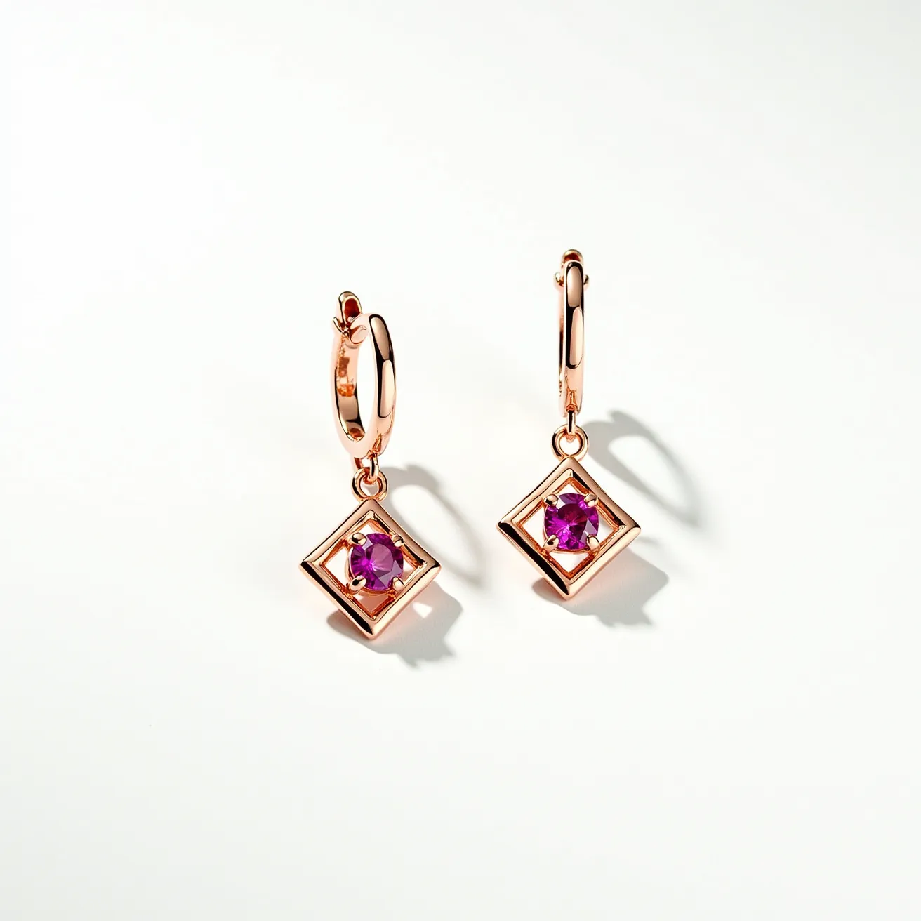 These pink earrings feature a delicate design with rose gold-colored metal, forming small hoops as the primary structure. Suspended from each hoop is a dangling element, characterized by a geometric, square-shaped frame enclosing a vibrant round-cut pink gemstone at the center. The gemstones are securely held in place by a prong setting, allowing the stones to catch and reflect light beautifully. The hoop clasp is of the hinged type, ensuring secure and comfortable wearing. The overall craftsmanship combines elegance with a contemporary touch, making these earrings an eye-catching accessory.