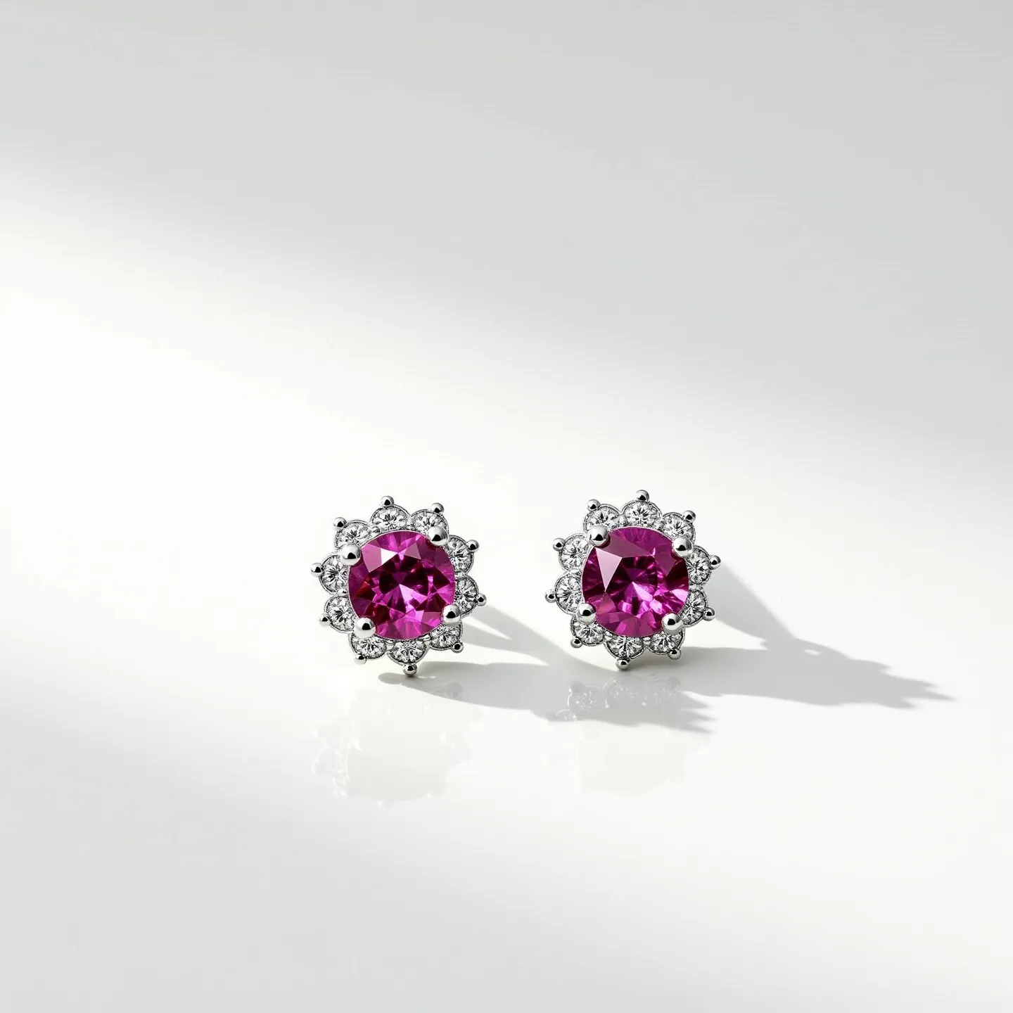 These pink sapphire earrings feature a central, round-cut pink sapphire as the focal point, surrounded by a halo of smaller, clear gemstones that are likely diamonds. The setting appears to be crafted from a polished metal, possibly white gold or platinum, which complements the vivid color of the sapphires. The stones are prong-set, enhancing their prominence and allowing light to enter from multiple angles for added brilliance. The design suggests a classic stud style, likely containing a push-back or butterfly clasp for secure attachment. The overall effect is a sophisticated and elegant piece of jewelry.