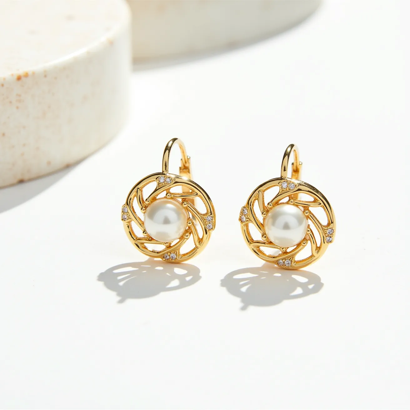 These post earrings feature a central round pearl, elegantly set in an intricate gold-toned swirl design. The surrounding gold structure is adorned with small, sparkling stones in a pave setting, adding a touch of glamour. These earrings use a latch-back clasp for secure attachment, making them both stylish and practical. The combination of the lustrous pearl and glittering stones against the rich gold tone creates a classic yet sophisticated look.