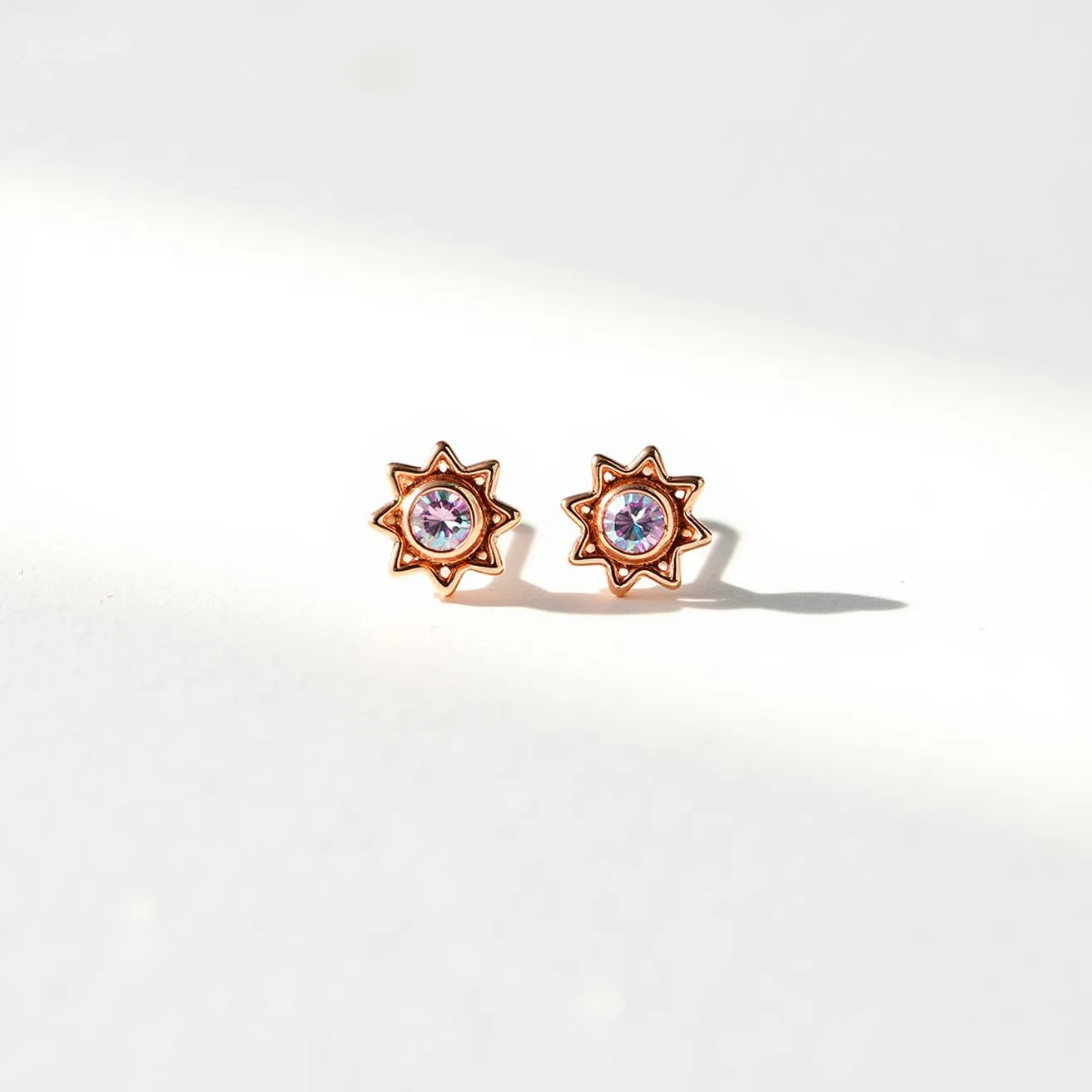 These post earrings showcase a beautiful star-like design with a central gemstone that appears to be set in a bezel setting. The gemstone has a round cut and exhibits a vibrant, multicolored sparkle, suggesting it may be an opal or a similar iridescent stone. The metal seems to be a warm-toned material, possibly rose gold or gold-plated, which complements the colorful gem. The earrings likely have a standard post and butterfly clutch attachment, securing them comfortably and stylishly in place.