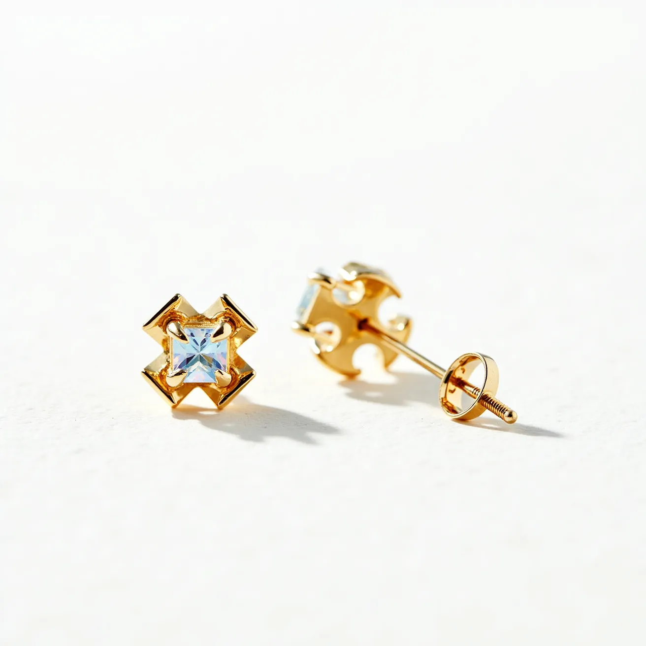 These post earrings feature a central square-cut gemstone with a brilliant, light-reflective finish. The stones are securely held in place by a meticulous prong setting that highlights their geometric shape. Surrounding the stones, the earrings are crafted from a polished gold metal that forms an intricate design adding to their elegance. The earrings are equipped with a screw-back post, ensuring they remain securely fastened when worn. The overall design combines classic elements with a contemporary twist, making these earrings both timeless and stylish.