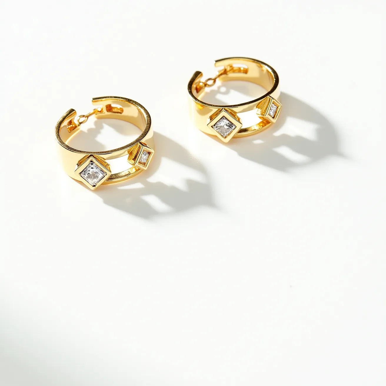 These ring earrings feature a set of hoop-style bands crafted from a shiny gold material. Embedded in each earring are three square-cut gemstones, likely diamonds or cubic zirconia, set in a bezel setting that accentuates their clarity and sparkle. The hoops are designed with a hinge clasp mechanism, ensuring secure and easy wear. The overall design combines elegance with a modern touch, making them suitable for various occasions.