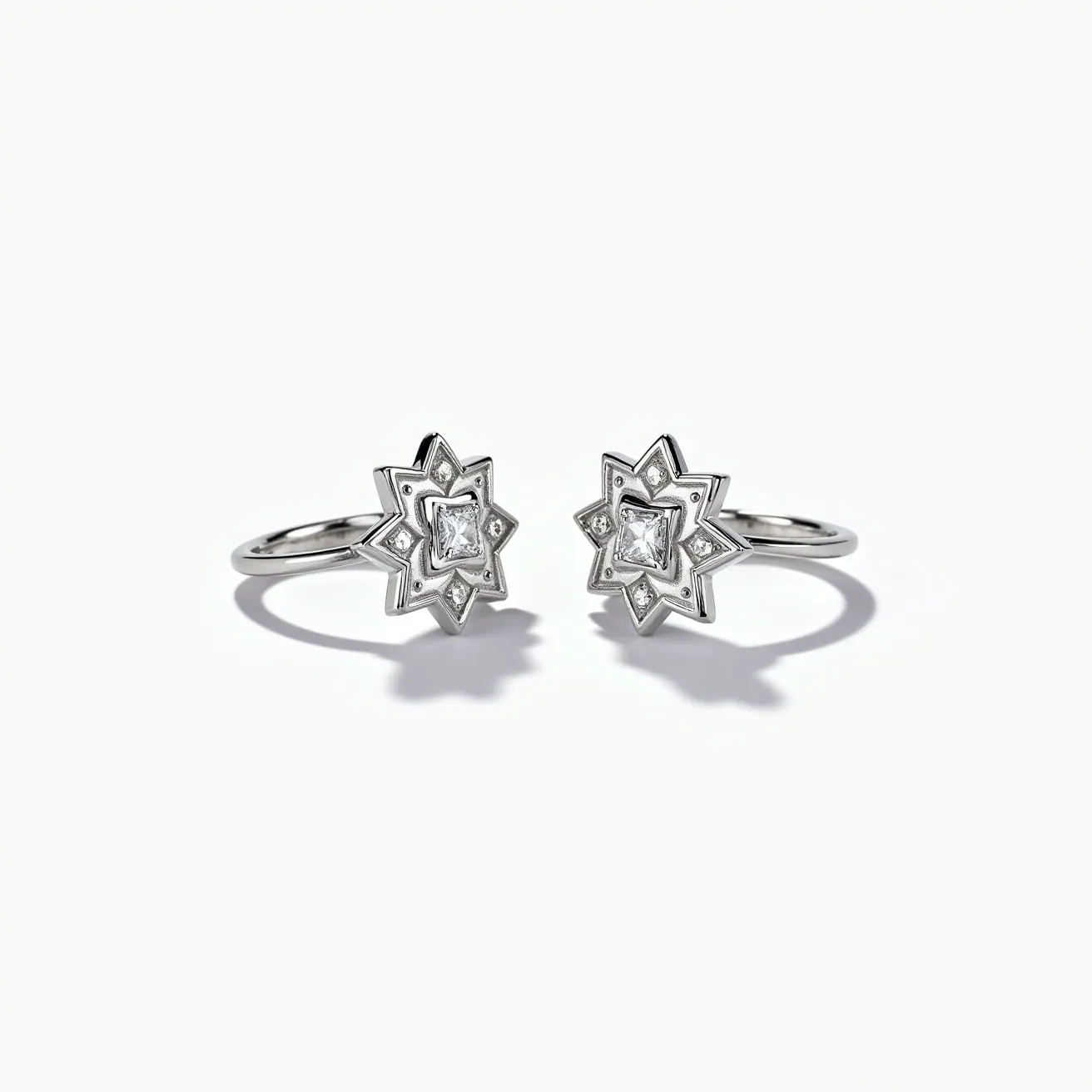 These ring earrings feature a star-shaped design crafted from a polished metal that likely resembles silver or white gold. At the center of each earring is a square-cut gemstone, which appears to be a diamond, set in a four-prong setting. The gemstone is surrounded by a geometric star pattern, adding a unique architectural flair. The earrings include a simple loop design for attachment, providing an elegant and secure clasp mechanism for wearing. The overall craftsmanship showcases a balance between modern design and classic elegance.