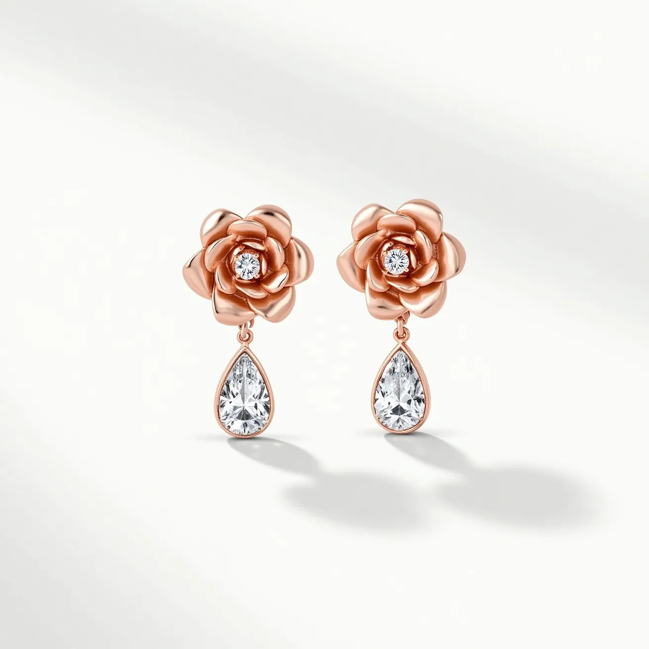 These rose earrings feature a delicate rose design crafted from a rose gold-toned metal, giving them an elegant sheen. At the center of each rose, a round-cut clear gem is securely set, adding a touch of sparkle. Dangling beneath the rose is a teardrop-shaped gem, also clear and faceted, enhancing the overall brilliance of the earrings. The teardrop gems are encased in a matching rose gold-toned setting that suspends them beautifully from the rose. These earrings likely use a post-back clasp for secure attachment to the ear, maintaining a cohesive and sophisticated design.