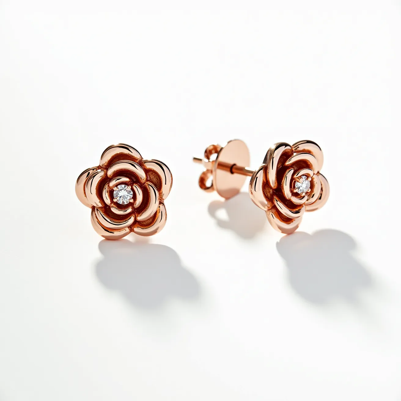 These rose earrings are crafted from a polished rose gold material, intricately shaped into the form of blossoming roses. At the center of each rose, a round-cut diamond or similar clear gemstone is meticulously set, adding a touch of elegance and sparkle to the design. The earrings feature a classic stud attachment, secured with a simple yet effective butterfly clasp, ensuring a comfortable and secure fit when worn. The combination of the lustrous rose gold and the clear gemstone creates a luxurious and sophisticated appearance, making these earrings a versatile accessory suitable for various occasions.