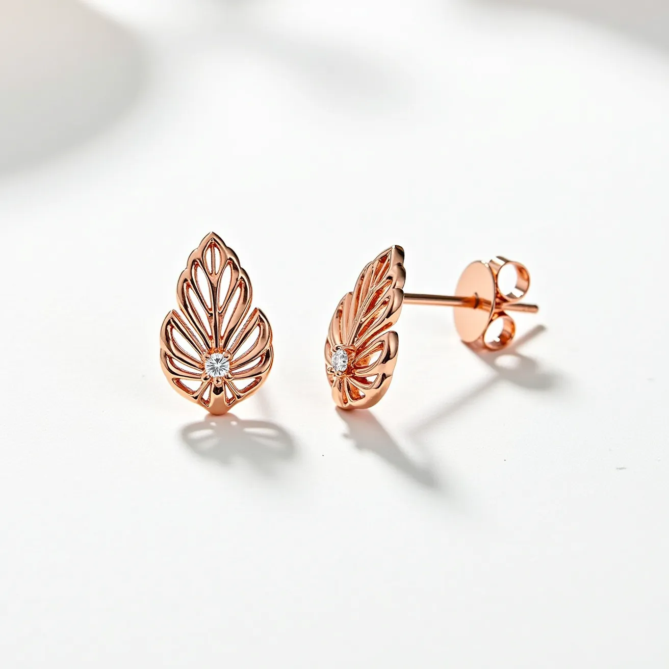 These rose gold earrings feature an intricate leaf-like design crafted from rose gold metal, accentuated by a single small round diamond at the center of each piece. The diamond is likely set in a prong setting to ensure secure placement while enhancing its brilliance. These earrings are equipped with a standard post and butterfly back clasp, offering a secure and comfortable fit for the wearer. The overall design combines elegance with a touch of nature-inspired artistry, making them a sophisticated accessory.