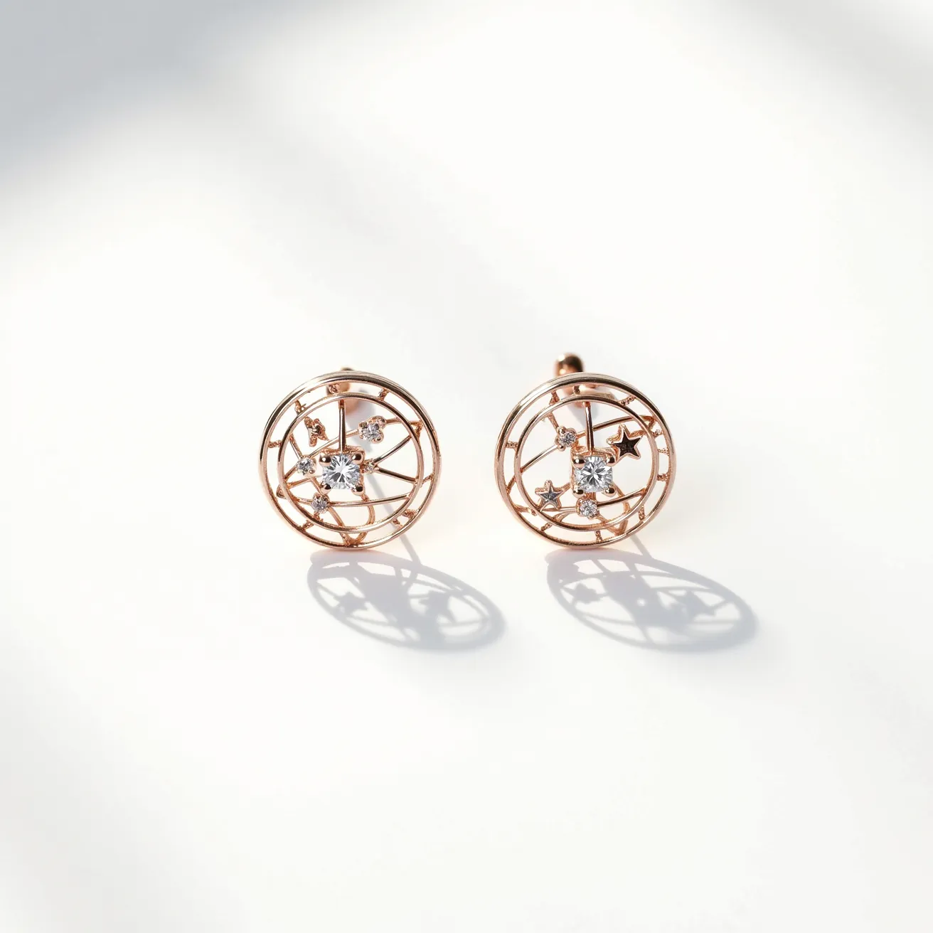 These rose gold earrings feature a delicate circular design, crafted from rose gold metal, exhibiting an intricate openwork pattern. At the center of each earring is a sparkling round-cut gemstone, likely a diamond or a similar transparent stone, securely set within a prong setting. Surrounding the central gem are additional smaller stones, also prong-set, adding a touch of brilliance and enhancing the overall aesthetic. The earrings appear to be secured with a post and butterfly clasp, ensuring both style and functionality for everyday wear.