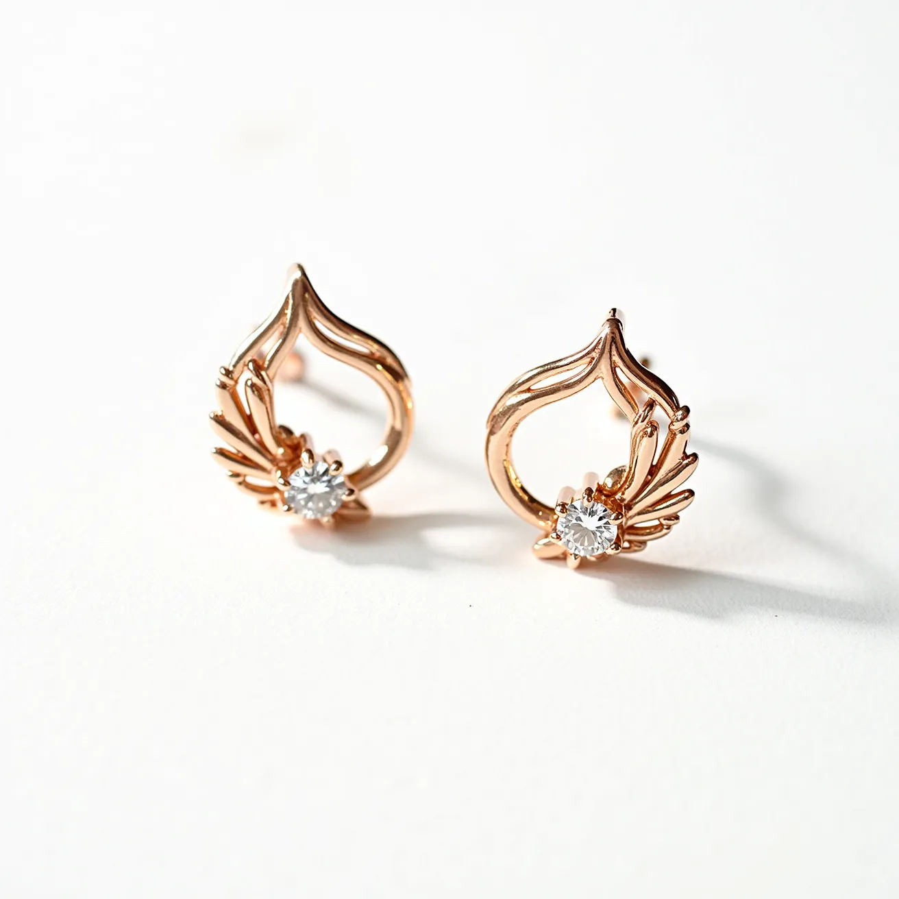 These rose gold earrings feature an intricate design shaped like stylized petals, crafted from rose gold metal that adds a warm and elegant glow. Each earring is adorned with a round-cut gemstone, likely a diamond or a similar clear stone, which is set prominently to enhance the overall sparkle. The setting securely holds the stones, providing a classic yet contemporary touch. The earrings are designed with a post back attachment, ensuring ease of wear and secure fastening for the wearer.