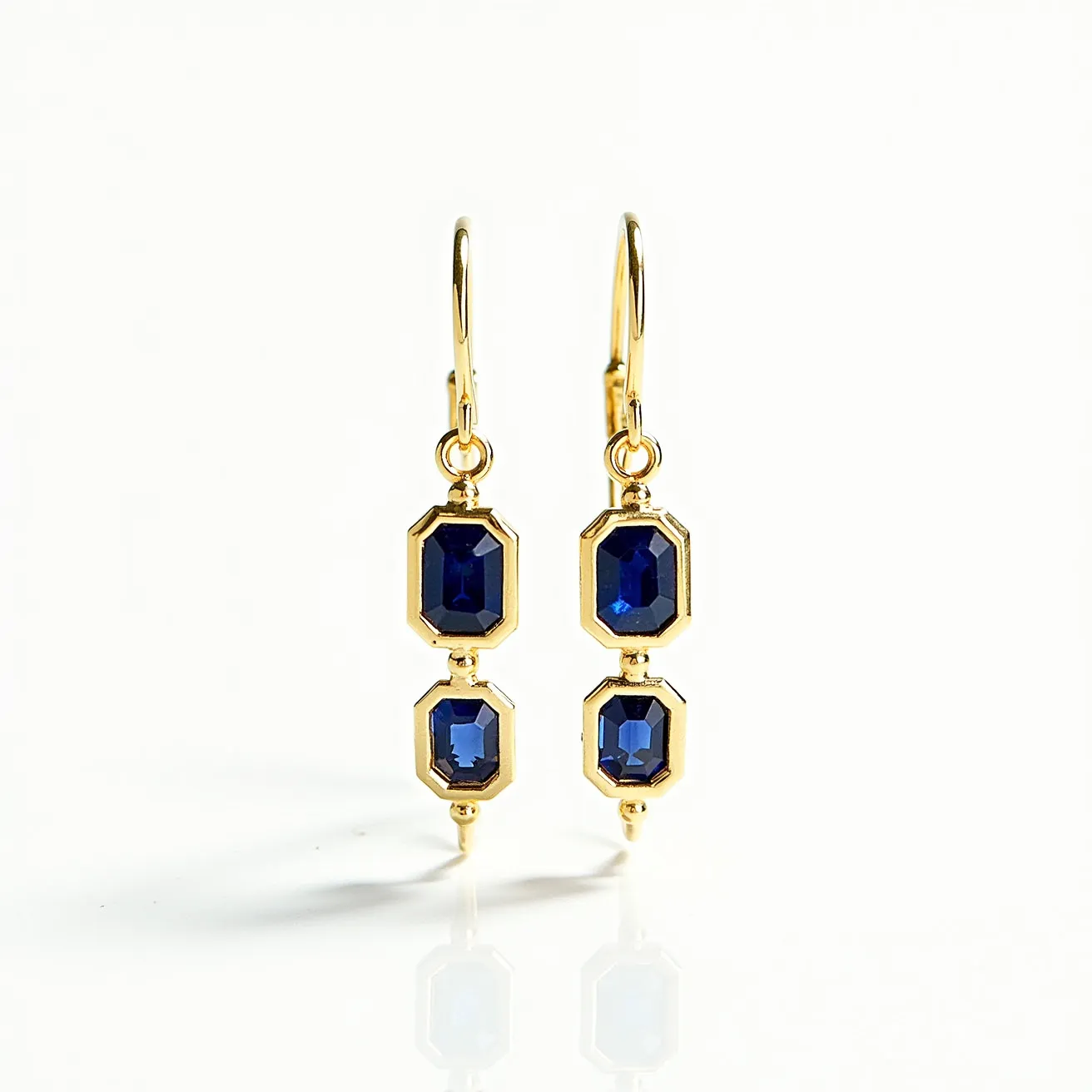 These sapphire earrings feature two stunning blue sapphires in each earring, cut in a classic emerald shape. The gemstones are set in a sleek gold frame that enhances their rich color. The earrings are designed with a simple hook clasp attachment, allowing for easy wear while adding an elegant touch. Each sapphire is securely set, showcasing meticulous craftsmanship and attention to detail in the overall design.