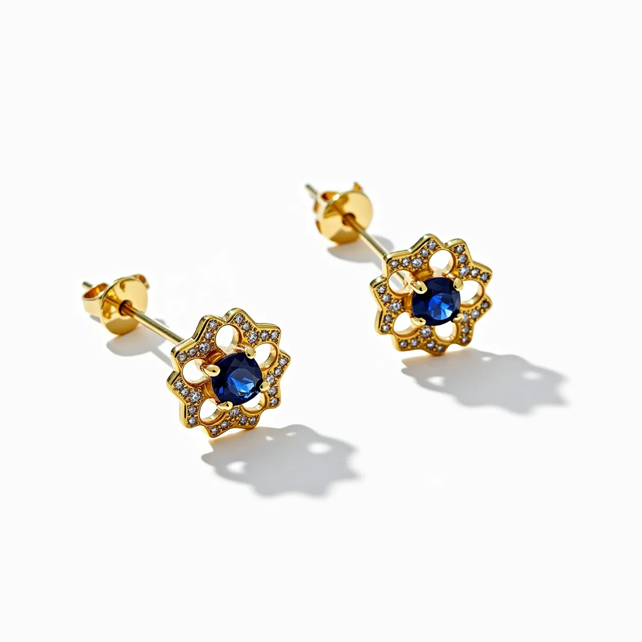 These sapphire earrings feature a central, deep blue sapphire gemstone, skillfully faceted to enhance its brilliance. The sapphire is set in a prong setting, surrounded by a floral-inspired design crafted from gold, which complements the rich color of the gemstone. The design is accentuated by smaller round-cut diamonds that encircle the central sapphire, adding an elegant sparkle. The earrings are secured with a classic post and butterfly clasp attachment, ensuring both style and comfort.