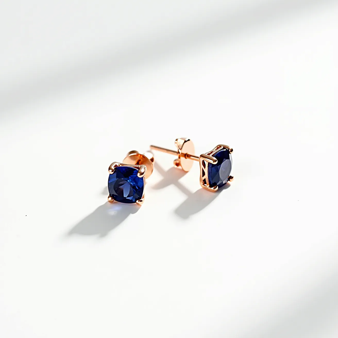 These sapphire earrings feature deep blue sapphires, each cut in a round shape that highlights their color and brilliance. The stones are secured in a four-prong setting made of a rose gold metal, which complements the rich hue of the sapphires. The earrings are designed as studs with a straightforward post and butterfly clutch back, ensuring a secure fit when worn. The choice of materials and design exudes elegance, making these earrings a timeless accessory.