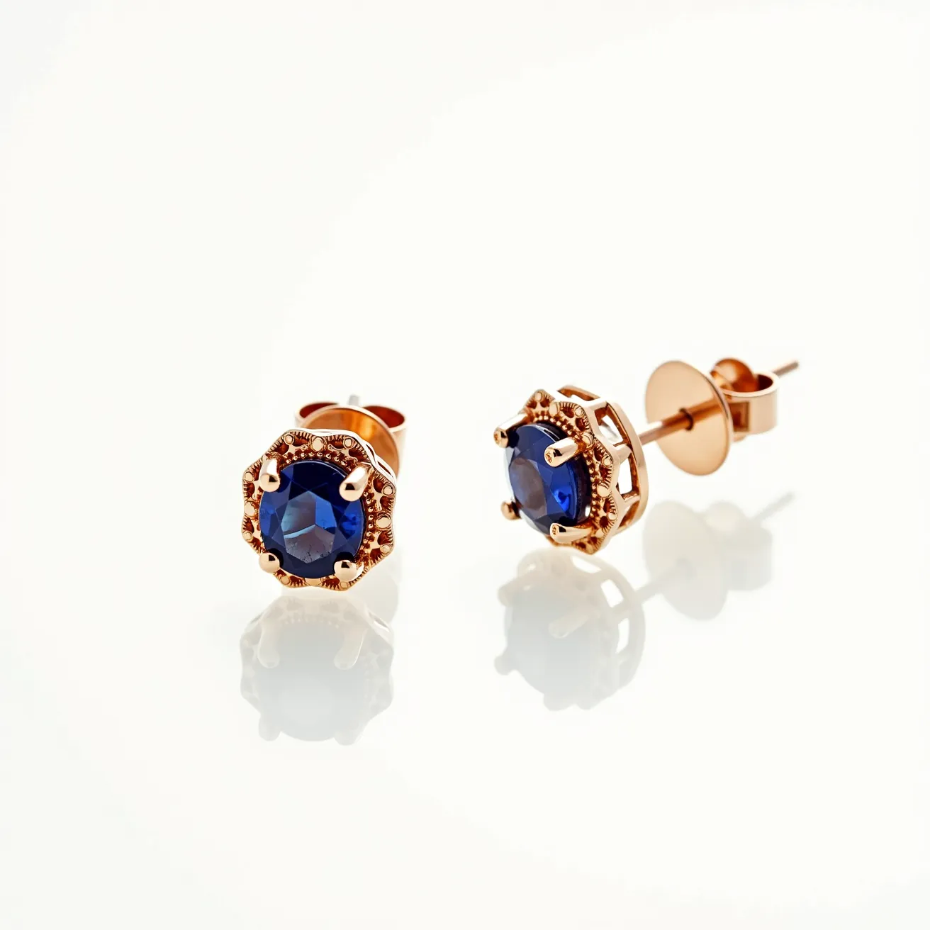 These sapphire earrings feature a stunning pair of deep blue sapphires, each cut in a round shape that enhances their brilliance and clarity. The sapphires are securely set in a six-prong setting, crafted from a warm, rose gold metal that highlights the richness of the stones. The intricate detailing around the prongs adds an elegant touch to the design. These stud earrings are equipped with a secure butterfly clasp, ensuring they stay comfortably in place when worn.