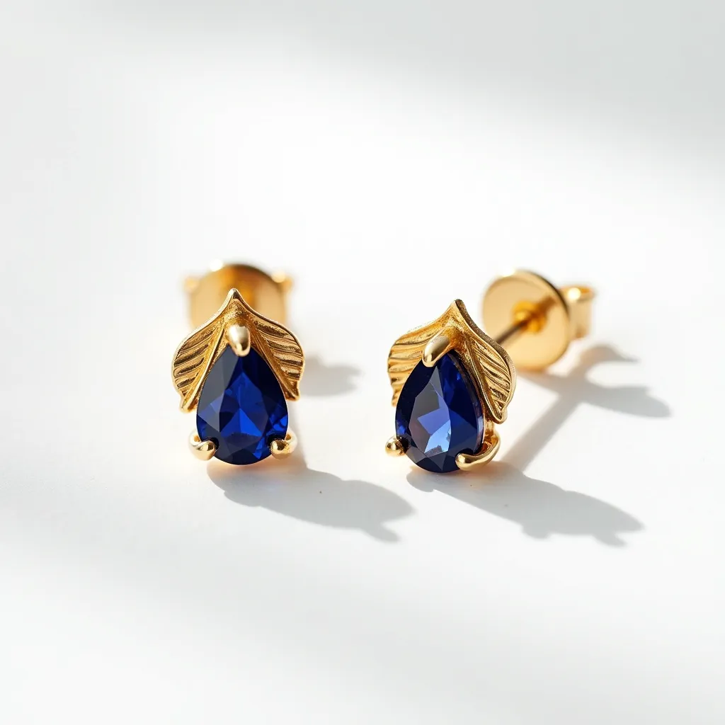 These sapphire earrings feature a beautifully cut pear-shaped sapphire as the centerpiece, set in a gold setting. The dark blue sapphires are elegantly held in place with delicate prongs, complemented by a leaf design on top, adding a touch of elegance to their appearance. The earrings are crafted in a gold-colored metal, which accentuates the deep blue of the sapphires. They use a classic stud post and butterfly clasp attachment to ensure they are secure when worn. The intricate design and choice of materials highlight the craftsmanship and attention to detail in these exquisite earrings.