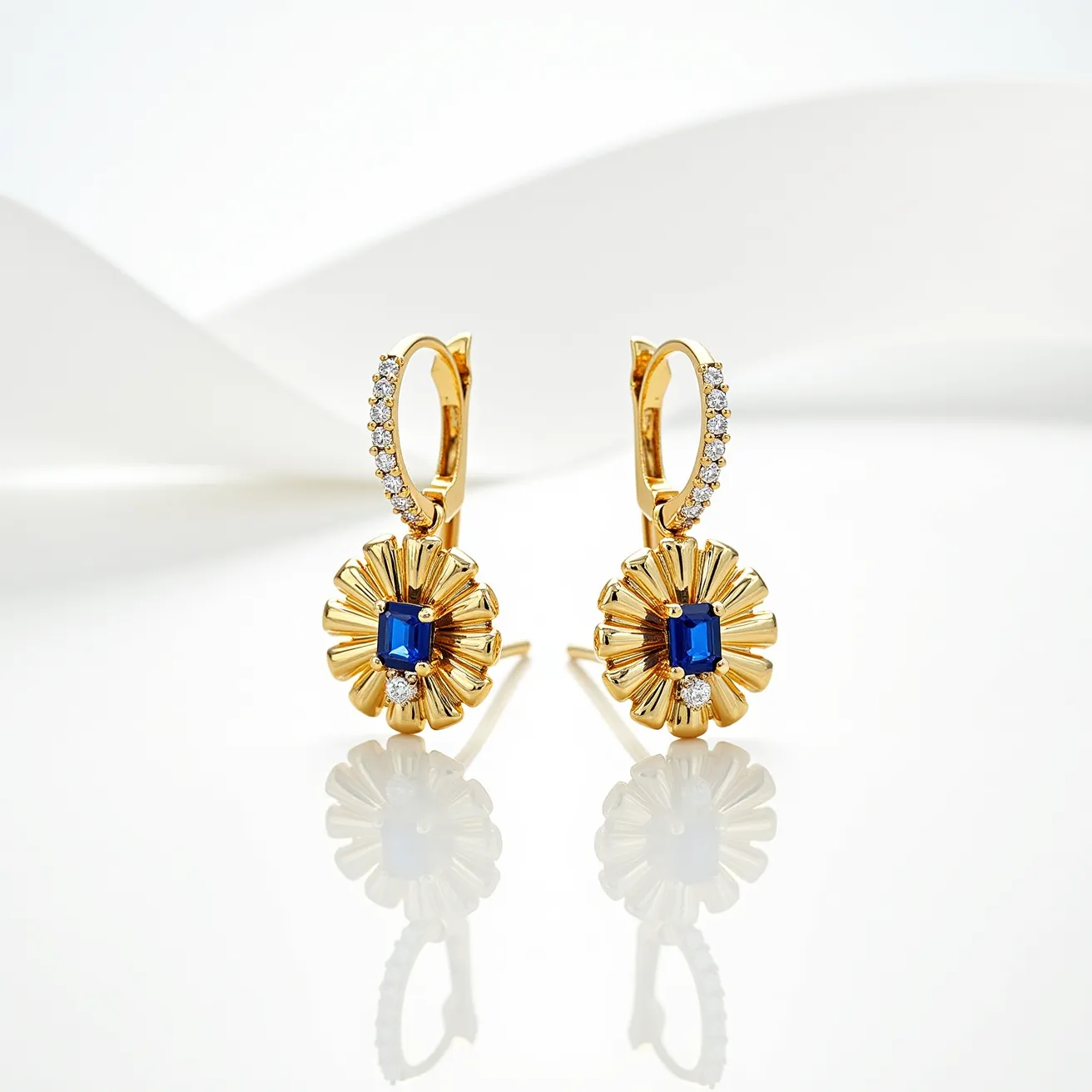 These sapphire earrings showcase a striking design featuring a central sapphire gemstone cut in a rectangular shape. The rich blue sapphire is set in a gold sunburst-style frame, which elegantly encircles the central stone. Surrounding the top curve of the earrings are small, round diamonds set in the gold, adding a touch of sparkle. These earrings are equipped with a hinged hoop clasp, providing a secure and stylish attachment. The combination of gold, sapphire, and diamonds creates a luxurious and refined aesthetic.