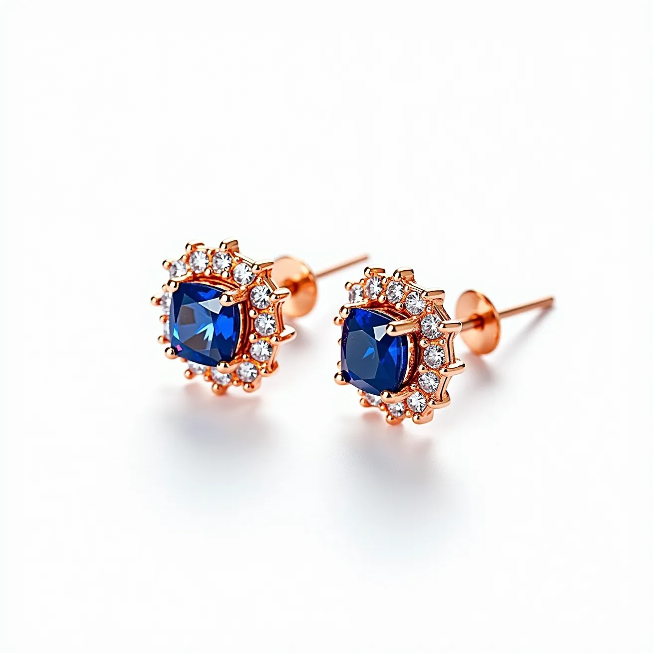 These sapphire earrings feature a striking central sapphire gemstone, beautifully cut to enhance its deep blue hue. The sapphire is surrounded by a halo of smaller, clear stones, likely diamonds, set in a circular pattern that amplifies the brilliance of the central stone. The setting is crafted from a metal that appears to be rose gold, adding a warm contrast to the cool tones of the sapphire and diamonds. The earrings utilize a stud post and butterfly clasp for secure and comfortable wear.