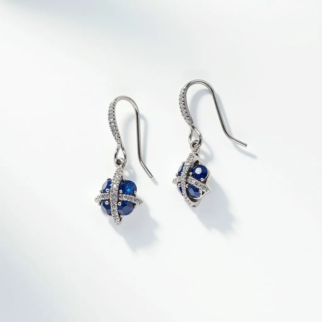 These silver dangle earrings feature a sophisticated design with a polished silver metal base that elegantly supports the gem settings. Adorned with deep blue gems, likely sapphires, each earring showcases multiple round-cut stones, artfully arranged in a clustered formation. These gems are accentuated by sparkling silver bands that crisscross around the cluster, enhancing the earrings’ luxurious appearance. The clasp style is a classic fish hook, ensuring a secure and comfortable fit, adding to the elegance and functionality of this exquisite piece.