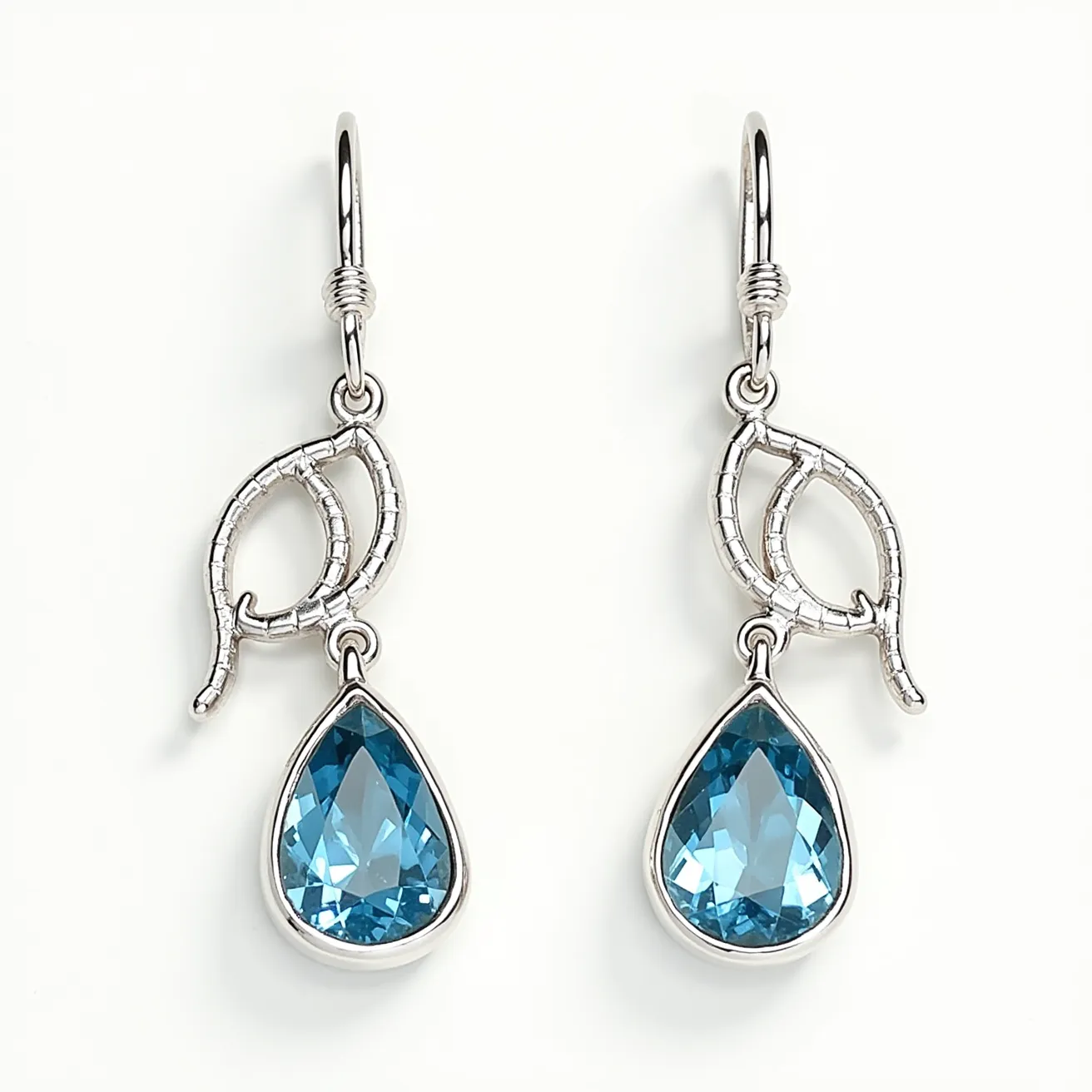 These silver drop earrings feature a pair of exquisite teardrop-shaped blue gemstones that are prominently showcased in a prong setting. The stones exhibit facets that enhance their sparkle, suggesting a possible faceted cut. Above the gemstones, a delicate leaf motif in silver adds an elegant and organic touch to the design. These earrings appear to use a hook clasp mechanism for attachment, providing ease of wear and a secure fit. The combination of the silver metalwork with the vibrant blue stones creates a striking contrast, perfect for adding a touch of sophistication to any ensemble.