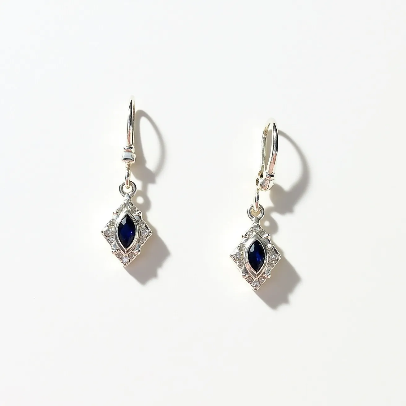 These silver drop earrings feature a lovely marquise-cut blue gemstone as the focal point, elegantly set within a rhombus-shaped frame adorned with smaller clear stones. The surrounding stones are likely set in a pavé style, adding a touch of sparkle to the overall design. The earrings are crafted in silver, providing a sleek and polished look. They are designed with a secure lever-back clasp, ensuring a comfortable and stable fit when worn. The combination of deep blue and silver makes these earrings a versatile and sophisticated accessory.