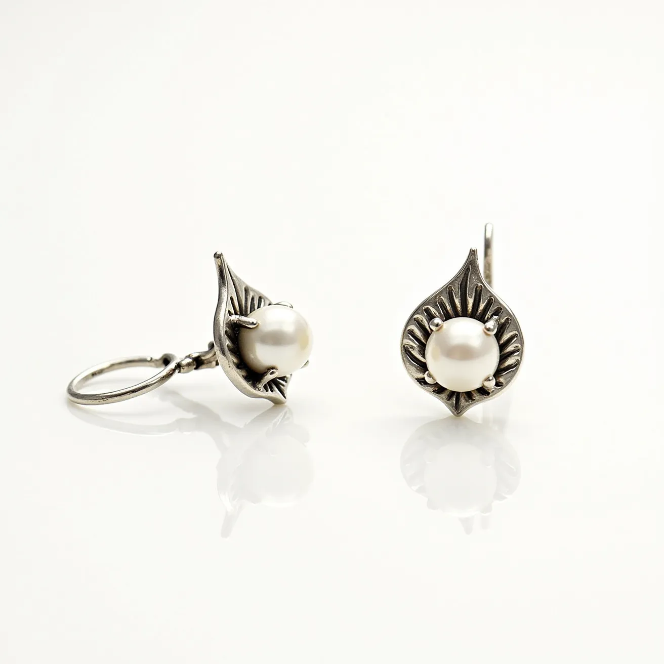 These silver earrings feature a classic and elegant design with a central pearl set in a bezel setting. The pearls are round and lustrous, complementing the silver's sheen beautifully. The earrings have an intricate leaf-like pattern on the silver surrounding the pearl, giving them a vintage and ornate appearance. The attachment is a secure hook clasp, ensuring they stay comfortably in place when worn. The combination of silver and pearl creates a timeless and sophisticated look suitable for various occasions.