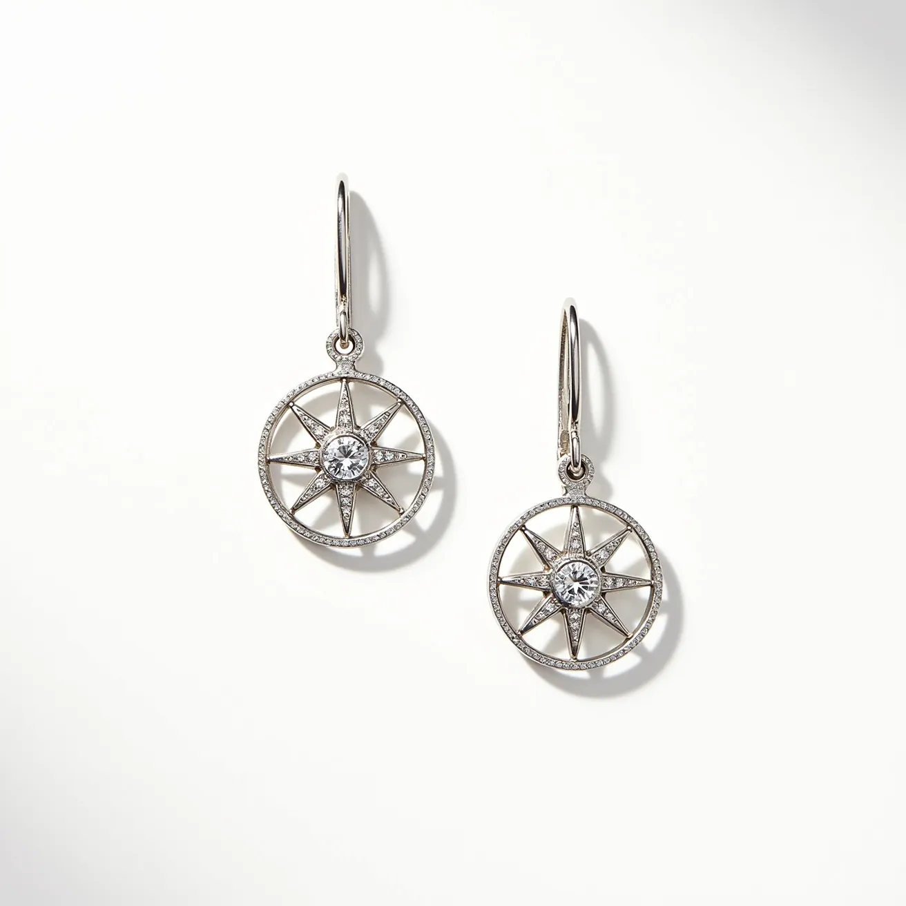 These silver earrings feature a round, openwork design resembling a compass rose, with a central brilliant-cut gemstone set in a bezel setting. The surrounding structure is artistically crafted from silver, enhancing the elegance of the design. The earrings are lightweight and dangle from simple and secure fishhook clasps, offering both style and ease of wear. The central stones are accentuated by smaller decorative elements, adding to the ornate and intricate aesthetic of the piece.