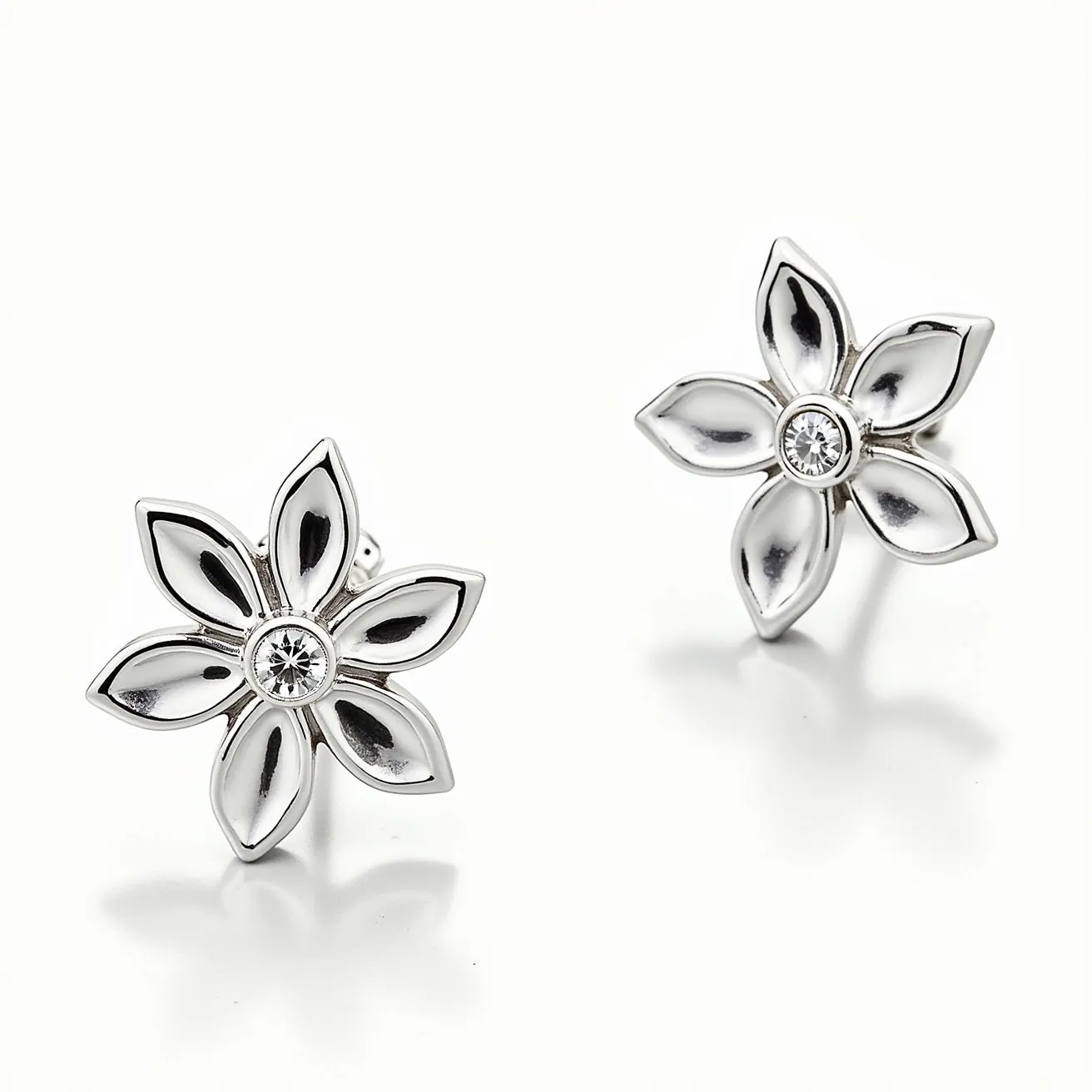 These silver earrings are designed in the shape of flowers, featuring a polished and refined finish that highlights their elegant form. At the center of each earring is a round-cut gemstone, possibly a diamond or cubic zirconia, set in a bezel setting, adding a touch of sparkle without overwhelming the design. The petals of the flower are crafted from silver, showcasing a smooth surface that enhances their delicate appearance. These earrings are likely designed with post backings, making them easy to wear and secure.