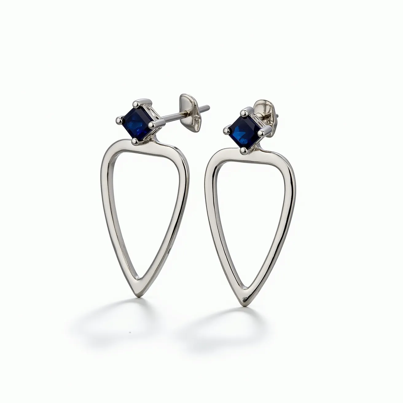 These silver earrings showcase an elegant and modern design, featuring a distinct teardrop shape crafted from polished silver. At the top of the earrings, there are square-cut blue gemstones set in a secure prong setting, adding a touch of sophistication and color contrast. The earrings are designed with a classic post and butterfly clasp attachment, ensuring a secure and comfortable fit. The combination of sleek silver and vibrant gemstones makes these earrings a versatile accessory for various occasions.