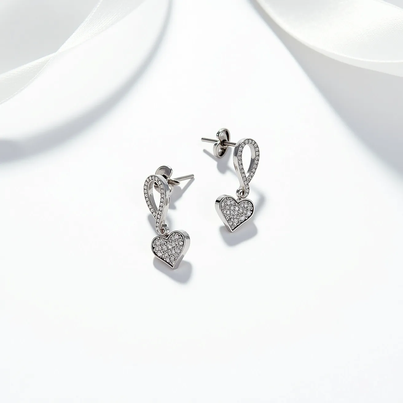 These silver heart earrings feature a delicate and elegant design, with each earring shaped like a heart crafted from sterling silver. The hearts are encrusted with small, round-cut gemstones, likely cubic zirconia or diamonds, that are pave-set to create a sparkling effect. The heart is attached to a stylized loop, also adorned with similar gemstones, adding a touch of sophistication. The earrings are secured with a post and butterfly clasp, making them both stylish and practical for pierced ears. The overall design presents a modern yet timeless appeal, perfect for a variety of occasions.