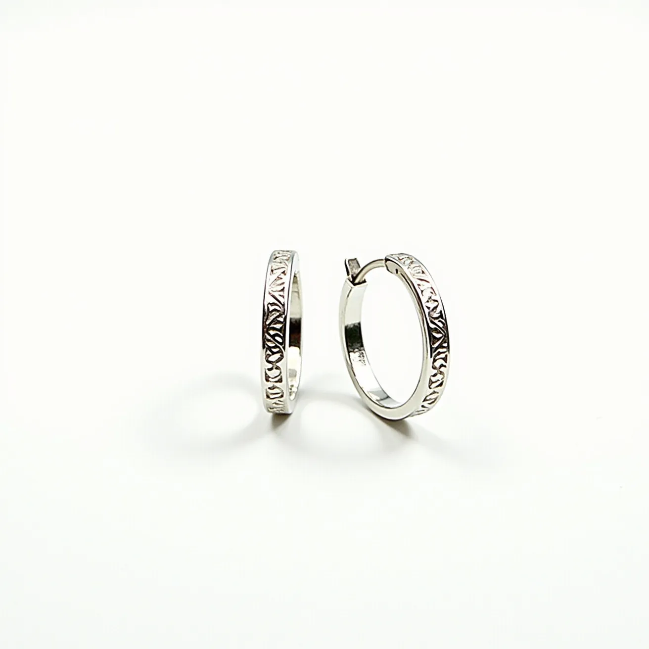 These silver hoop earrings feature a polished metal finish with intricate engraved patterns along the surface, adding a touch of elegance and complexity to their design. The hoops are made primarily of silver, giving them a sleek and shiny appearance. They are crafted with a hinge and snap closure mechanism, providing a secure and comfortable fit when worn. The overall look is simple yet sophisticated, making these earrings a versatile accessory for various occasions.