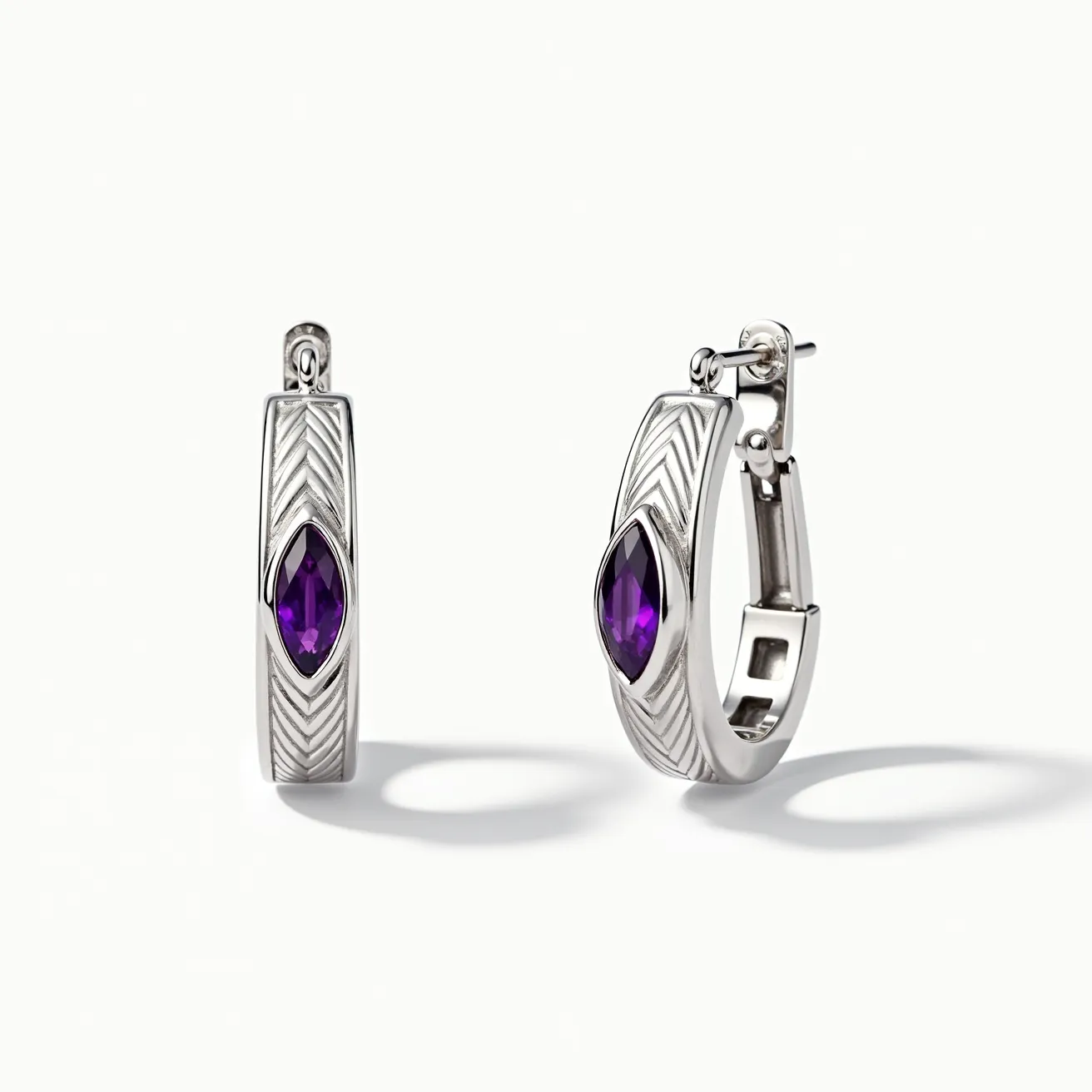 These silver hoop earrings feature a sleek metallic design with an elegant chevron pattern etched along the surface. A striking marquise-cut purple gemstone is set within each earring, adding a vibrant splash of color that stands out against the silver backdrop. The earrings are secured with a hinged clasp, providing ease of use and ensuring they remain comfortably in place. The combination of silver and the deep purple stone creates a sophisticated and modern aesthetic.