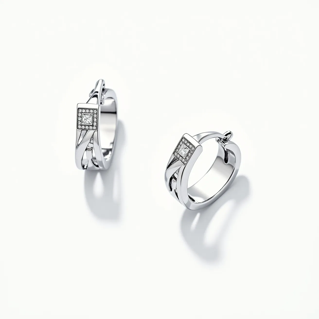 These silver hoop earrings feature a sleek and polished design, made entirely from a shiny silver metal that adds a touch of elegance. Each earring is adorned with a square-shaped gemstone, likely a clear gem such as a diamond or cubic zirconia, which is cut with precision and set within a subtle square bezel. The gemstones are held in place securely, enhancing the sophisticated look of the hoops. These earrings are designed with a hinged back clasp, ensuring ease of use while providing a secure fit when worn. The careful attention to detail and the integration of the gemstone setting add a classic yet contemporary flair to the overall design.