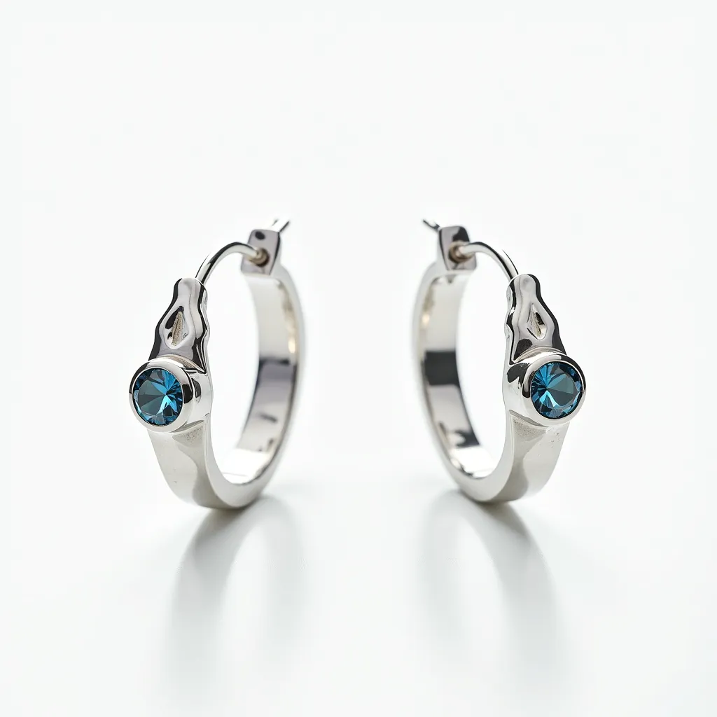 These silver hoop earrings exhibit a sleek, polished design crafted from high-quality silver, presenting a modern aesthetic. Each earring is embellished with a round, brilliant-cut blue gemstone, securely set in a bezel setting which highlights the stone's vibrant hue while ensuring durability. The hoops feature a hinged clasp, allowing for easy and secure attachment to the ear. The elegantly designed detail above the gemstone adds a touch of sophistication, enhancing the overall allure of these stylish accessories.