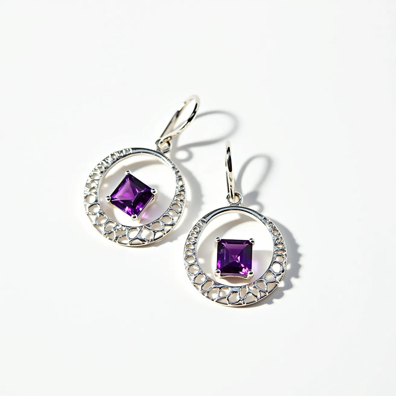 These silver hoop earrings feature a modern and elegant design, crafted from sterling silver with intricate openwork detailing on the hoops. At the center of each hoop is a striking square-cut, purple gemstone set in a four-prong setting, adding a vibrant pop of color. The earrings are secured with a sleek lever-back clasp, ensuring both style and security for the wearer.