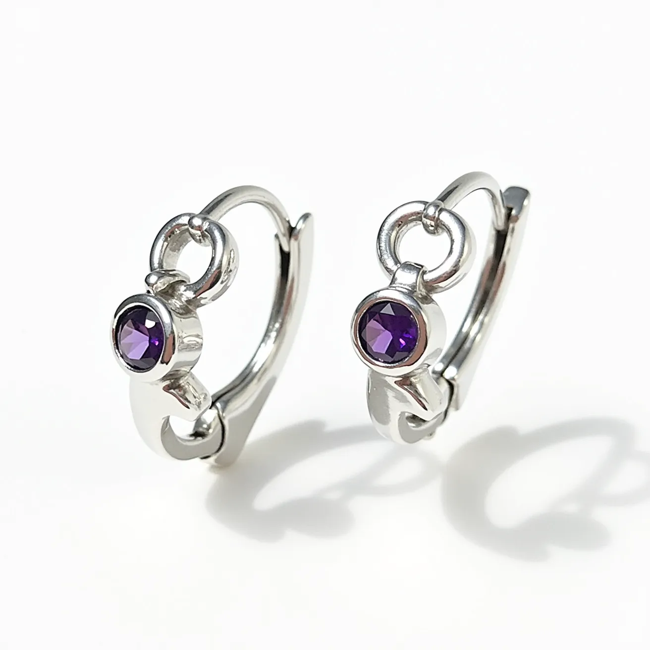 These silver huggie earrings feature a sleek, polished finish that highlights their elegant design. Each earring is adorned with a vivid purple gemstone, which appears to be amethyst, cut in a round shape and securely set in a bezel setting that enhances its color and brilliance. The earrings have a hinged clasp mechanism, providing a secure and convenient closure. The overall craftsmanship combines simplicity and sophistication, making these earrings a versatile accessory for various occasions.