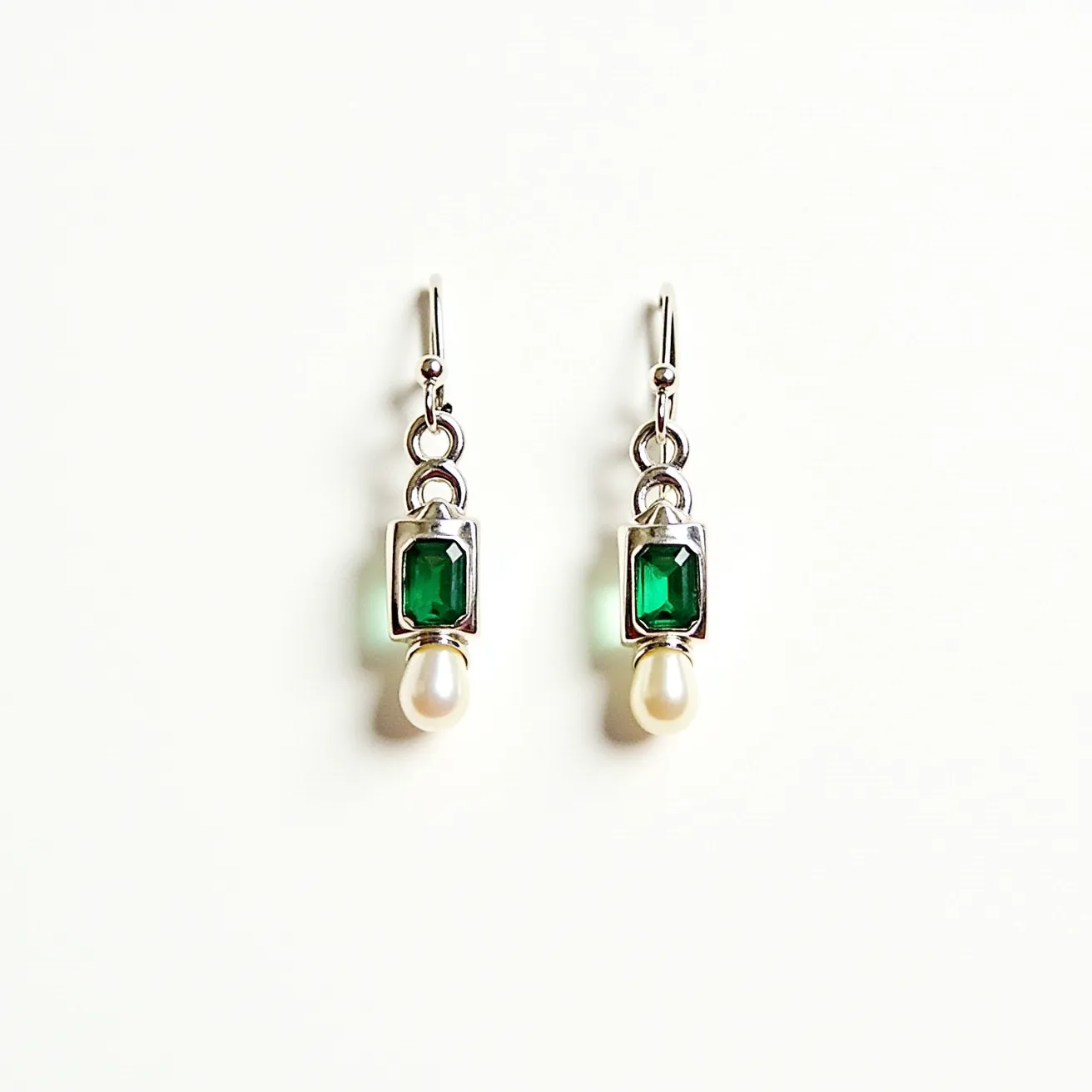 These silver huggie earrings feature a sleek design with a rectangular green gem, likely an emerald cut, set securely in a polished bezel setting. Below the green gem, there is a drop-shaped pearl that adds an element of elegance and contrast to the overall look. The earrings use a simple hook clasp for easy attachment and removal, ensuring both security and comfort when worn. The use of silver as the primary material highlights the vibrant colors of the gems, making these earrings a stylish and sophisticated accessory.