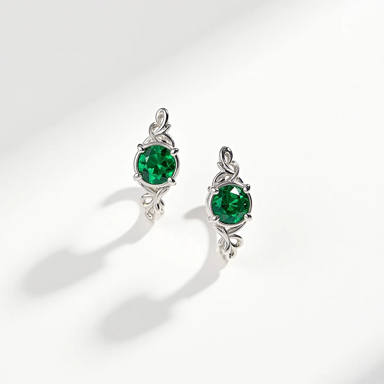 These silver stud earrings feature a radiant green gemstone, which appears to be a round-cut stone, elegantly set in a prong setting. The silver framework around the gemstone includes intricate, swirling details that enhance the overall design. The earrings are likely secured with a typical post and butterfly clutch back, ensuring a snug fit when worn. The combination of the vibrant green gem with the delicate silver embellishments creates a striking and stylish appearance.