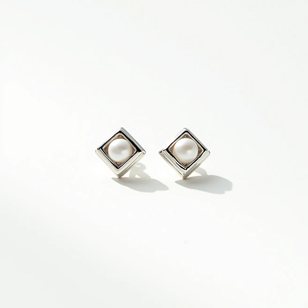 These silver stud earrings feature a refined design with a central round pearl set in a square mount. The pearls are smoothly polished, adding a touch of elegance to the overall appearance. Surrounding the pearls, the square setting is crafted from silver, providing a sleek and modern frame that enhances the luster of the pearls. The attachment is designed as a simple post, suitable for secure and comfortable wear. These elements together create a stylish accessory that is both contemporary and classic.