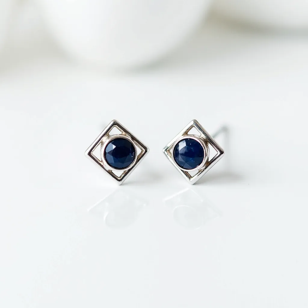 These silver stud earrings feature a modern geometric design highlighted by a square silver frame. At the center of each stud is a round, faceted dark blue gemstone, elegantly set to create a striking contrast with the silver. The stones are securely held within a bezel setting, adding to the sleek aesthetic. These earrings are designed with conventional posts, likely to be secured with friction backs, offering both style and ease of wear.