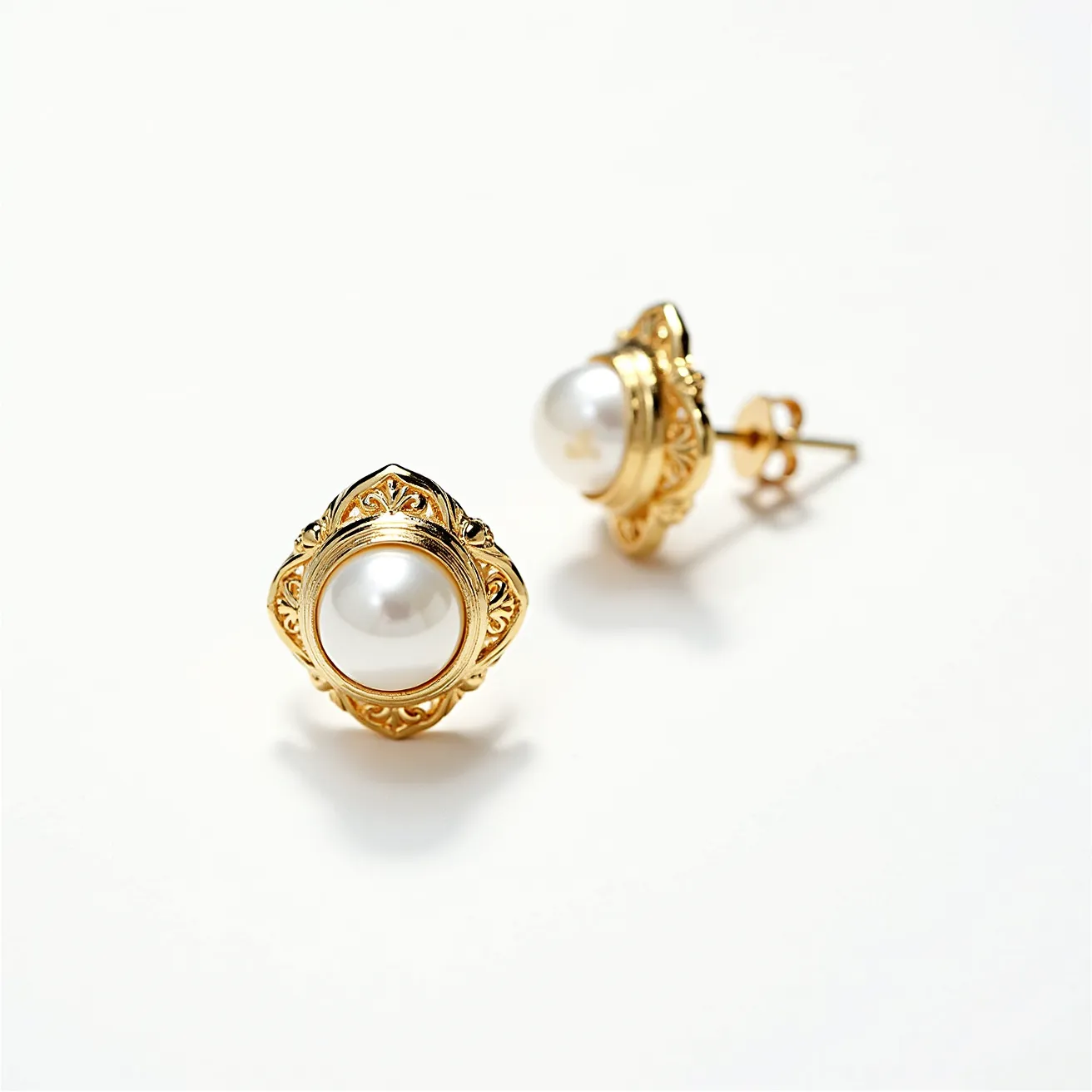 These pair of small earrings features a classic and elegant design, with each earring showcasing a prominent white pearl at its center. The pearls are smooth and spherical, elegantly set in a gold-toned frame that highlights their lustrous appeal. Surrounding the pearls is intricate goldwork with ornate, decorative engravings that add a touch of vintage sophistication. The earrings utilize a post-back clasp, ensuring a secure and comfortable fit when worn. The combination of the rich gold color with the pristine white of the pearls creates a timeless look that can complement various styles.