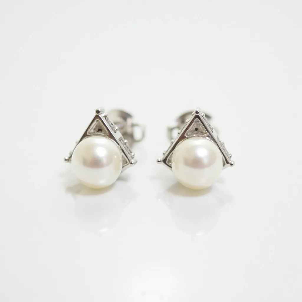 These small earrings feature a central round pearl, exhibiting a lustrous white sheen, elegantly set within a triangular metallic frame. The frame appears to be crafted from a polished metal, likely silver, that complements the pearl's opalescent surface. Each earring is designed with small, stud-like embellishments at each point of the triangular frame, adding subtle detail to the overall design. These earrings secure with a classic stud post and butterfly clasp, making them both stylish and practical for everyday wear.