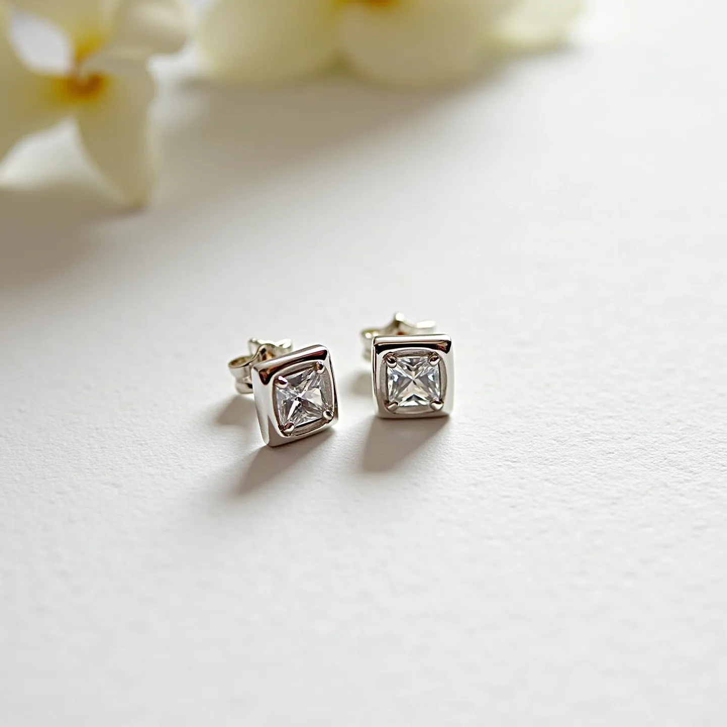 These square earrings feature a sleek, modern design with a polished metal setting, likely made of silver or white gold, which provides a reflective and elegant appearance. Each earring showcases a square-cut gemstone, possibly a diamond or a high-quality cubic zirconia, that is precisely set within a bezel setting, ensuring both security and a clean aesthetic. The post-style attachment indicates they are designed for pierced ears, with butterfly or friction backs that offer secure and comfortable wear. The overall minimalist design emphasizes the clarity and cut of the stones, making these earrings an excellent choice for both everyday wear and special occasions.