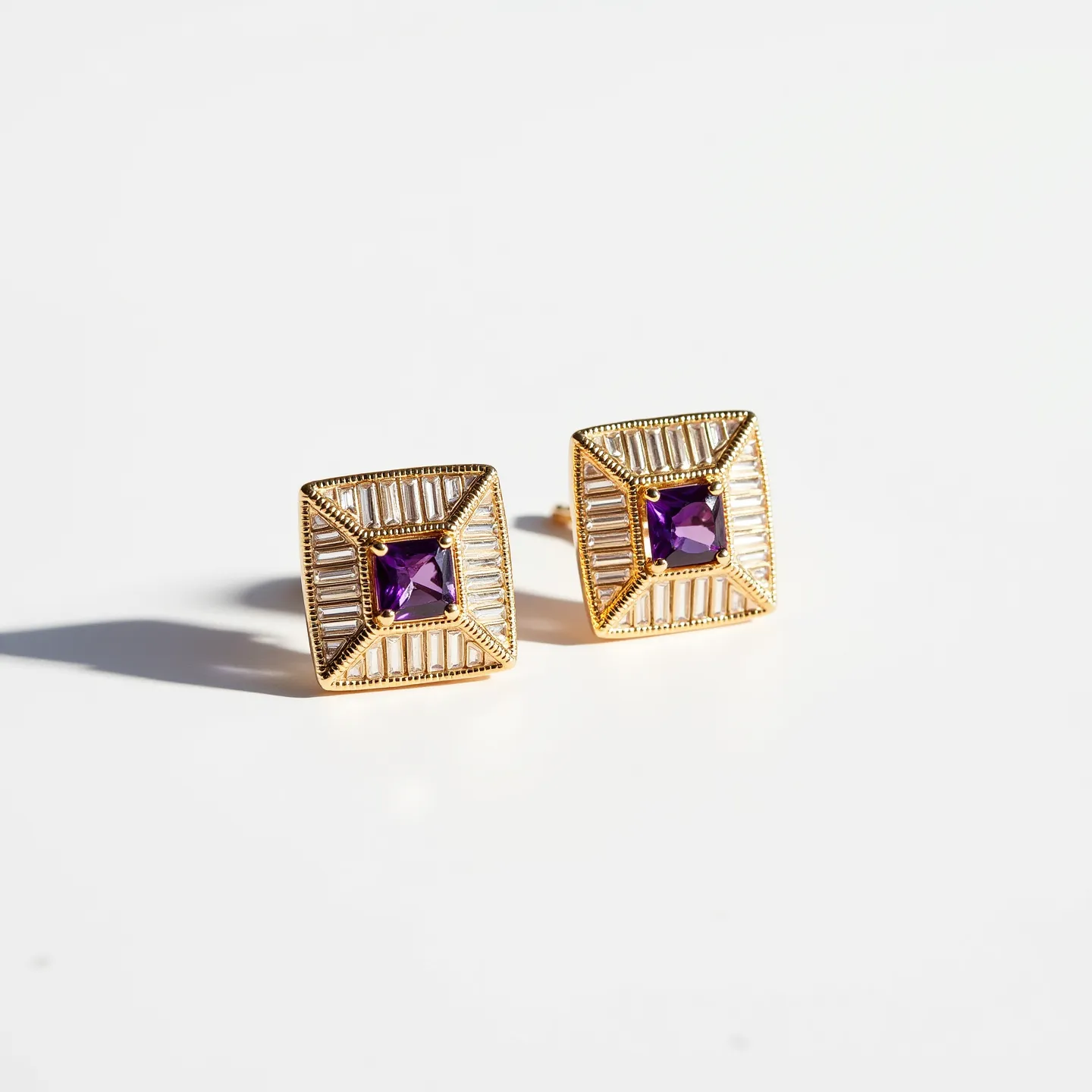 These square earrings feature a striking design with a prominent central gemstone, likely an amethyst, cut in a square or princess style. The stone is encased in a bezel setting, ensuring its security and adding to its elegance. Surrounding the gemstone is a detailed gold framework with geometric patterns, contributing to a luxurious aesthetic. The attachment mechanism appears to be a traditional post and push-back clasp, ensuring a secure and comfortable fit for the wearer. The combination of gold and the purple gemstone creates a classic and sophisticated look, suitable for various occasions.