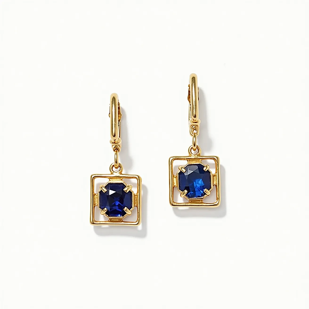 These square earrings feature a gold-toned metal frame with an elegant and simple design. At the center of each earring is a deep blue gemstone, likely a sapphire, which is cut in an octagonal shape to maximize its brilliance. The stones are securely held in place by four prongs at the corners, enhancing their visual prominence while ensuring stability. These earrings are equipped with a leverback clasp, providing a secure and comfortable fit for the wearer. The combination of the rich blue sapphires and golden setting creates a classic and sophisticated look.